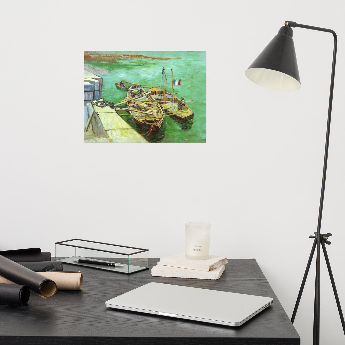 Van Gogh's 'Quay with Men Unloading Sand Barges' on a 12"x16" unframed poster print on a white wall above a modern office desk, lamp, and assorted desk items.
