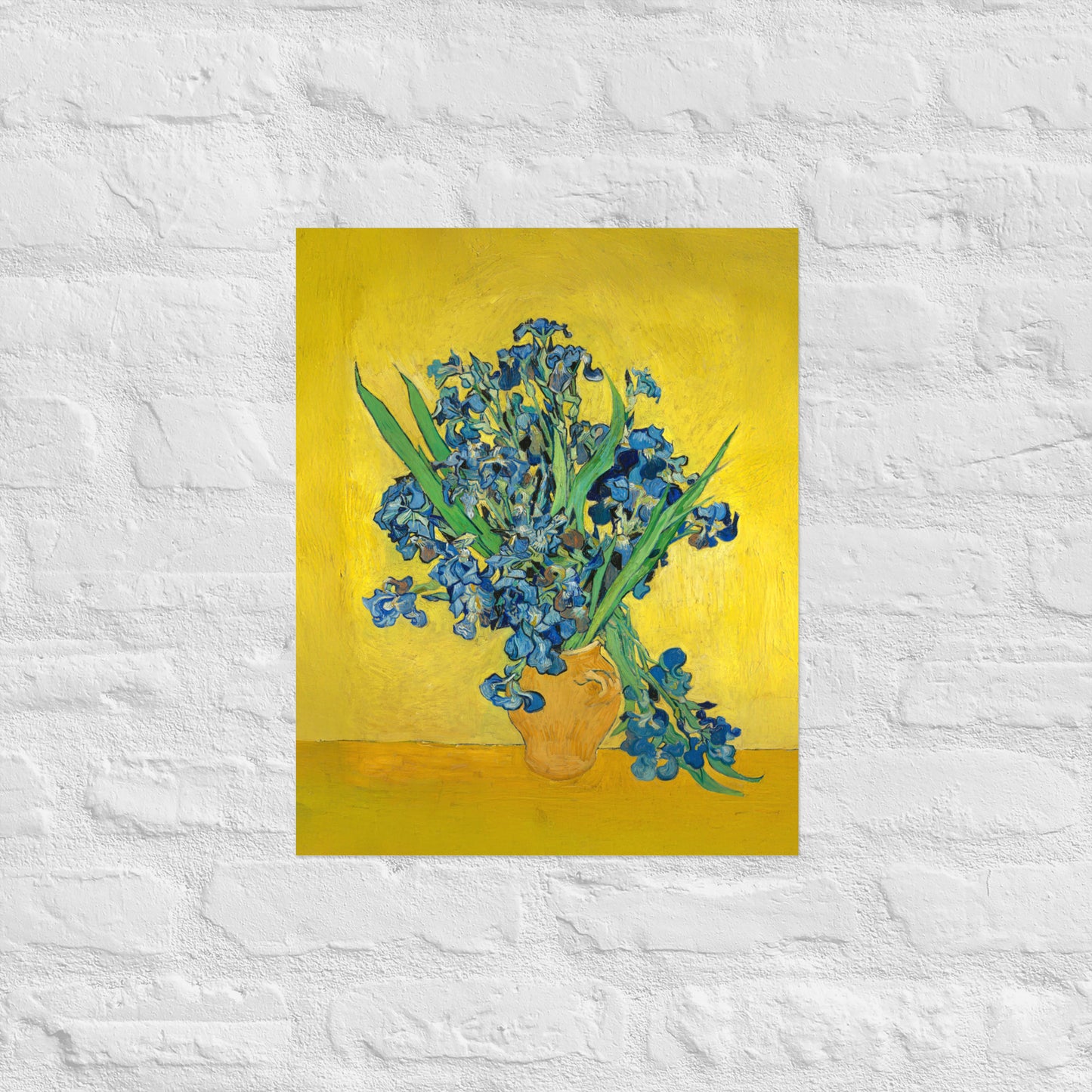 Van Gogh's 'Vase with Irises Against a Yellow Background' on a 16"x20" unframed poster print on a white brick wall.