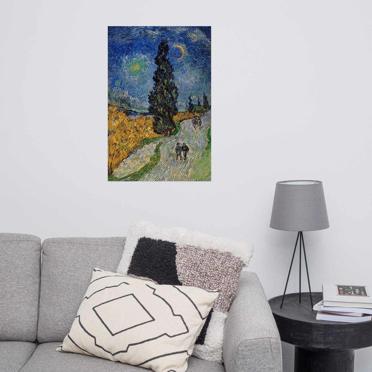 Van Gogh's 'Road with Cypress and Star' on a 24"x36" unframed poster print on a white wall above a gray sofa with throw pillows and side table with a lamp.