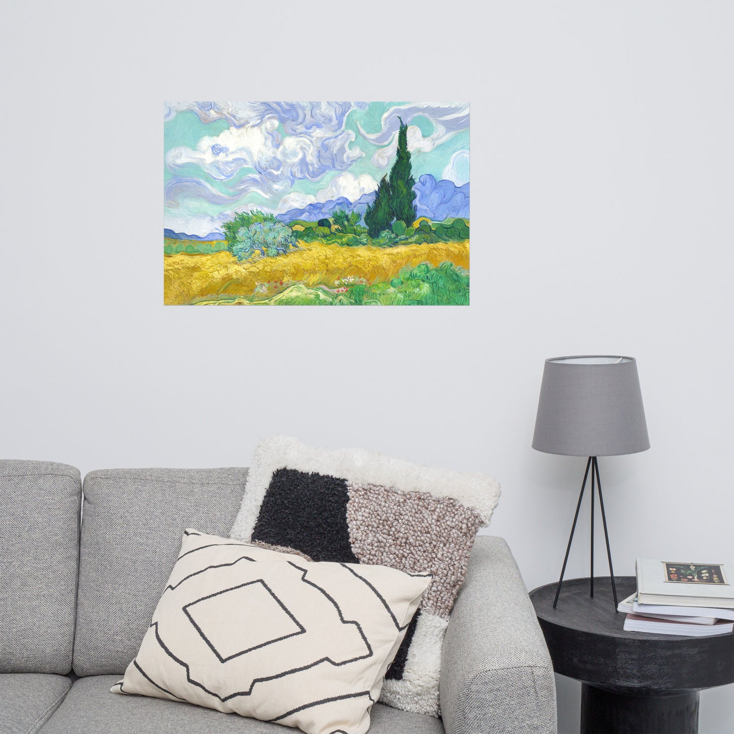 Van Gogh's 'Wheat Field with Cypresses' on a 24"x36" unframed poster print on a white wall above a gray sofa with throw pillows and side table with a lamp.