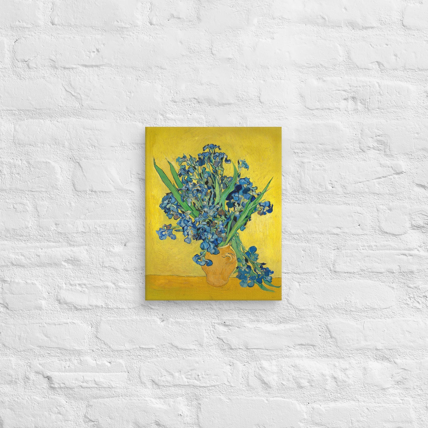 Van Gogh's 'Vase with Irises Against a Yellow Background' on a 11"x14" unframed canvas print on a white brick wall.