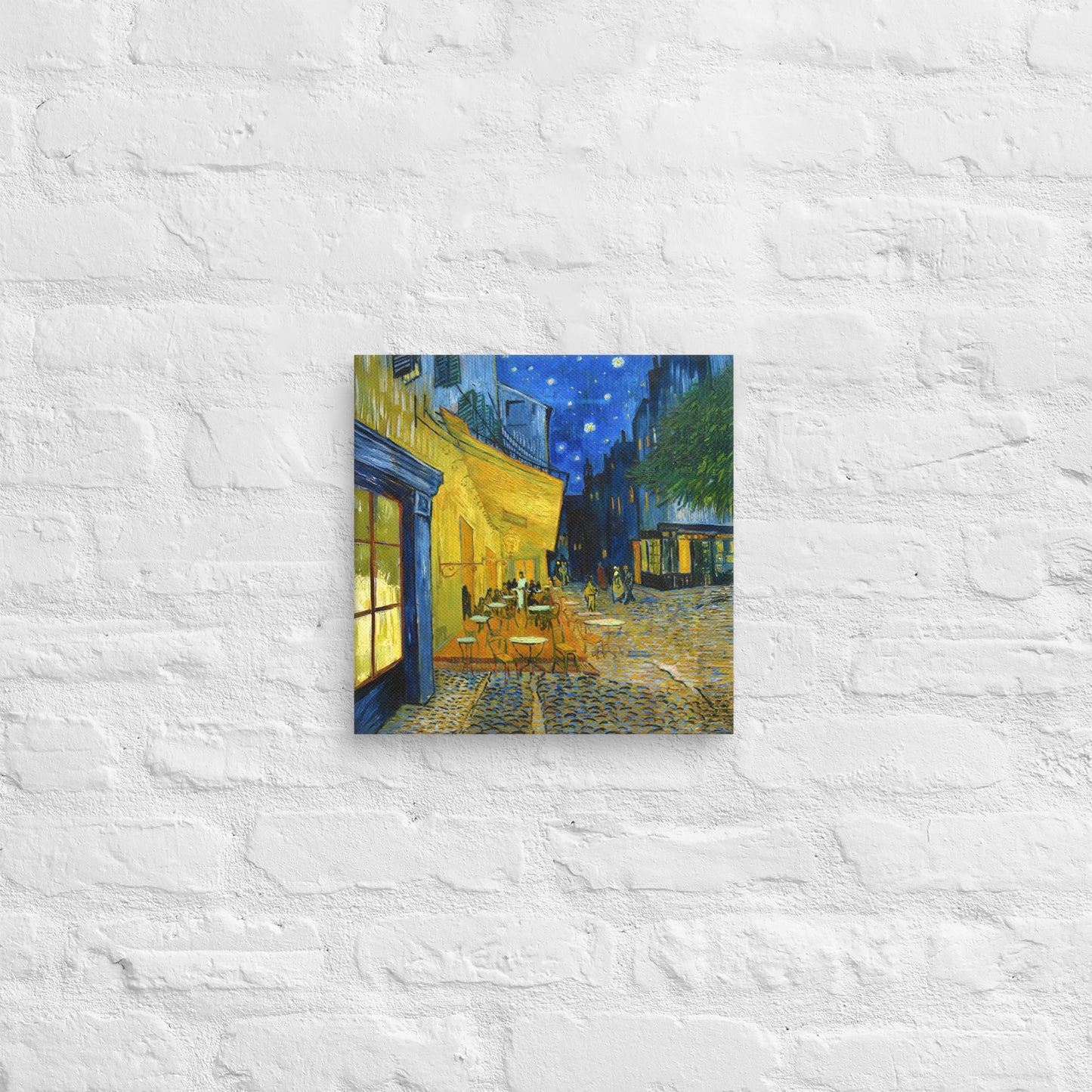 Van Gogh's 'Café Terrace at Night' on a 12"x12" unframed canvas print on a white brick wall.