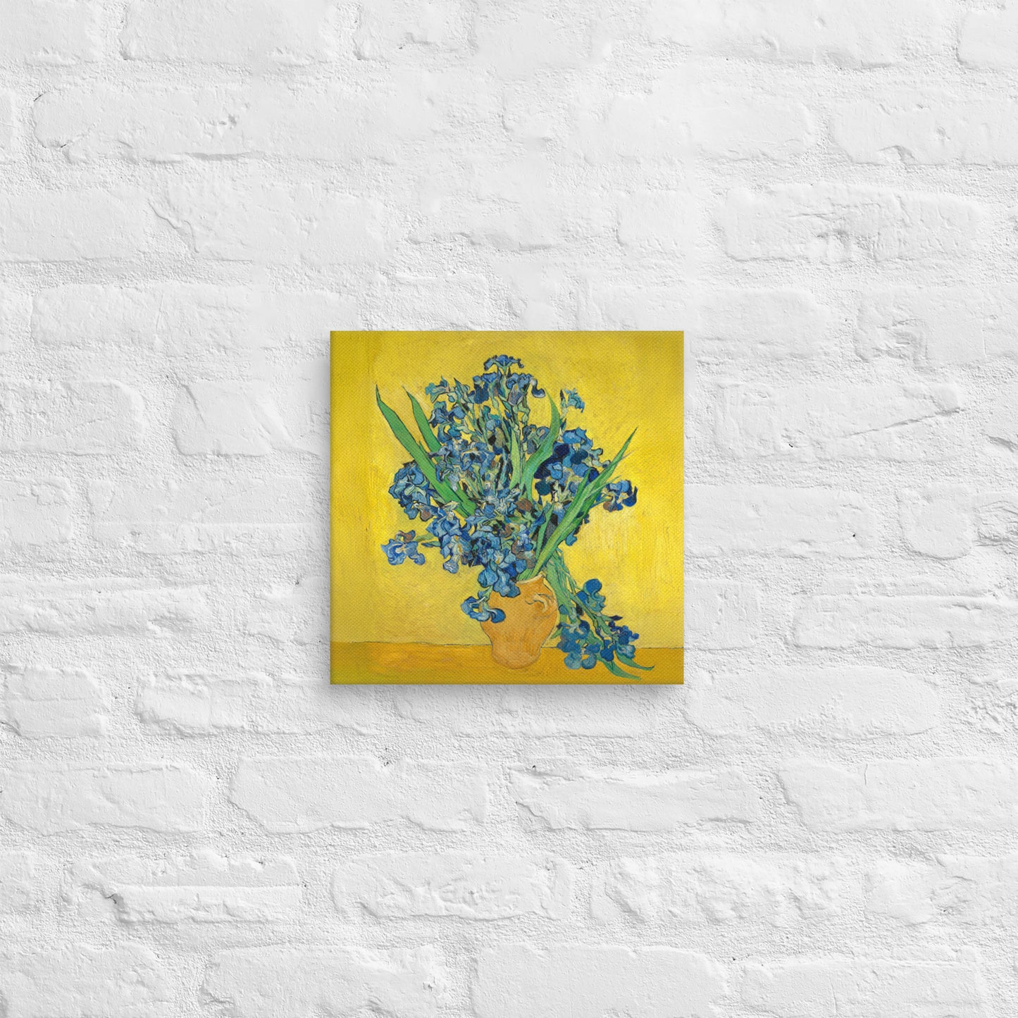 Van Gogh's 'Vase with Irises Against a Yellow Background' on a 12"x12" unframed canvas print on a white brick wall.