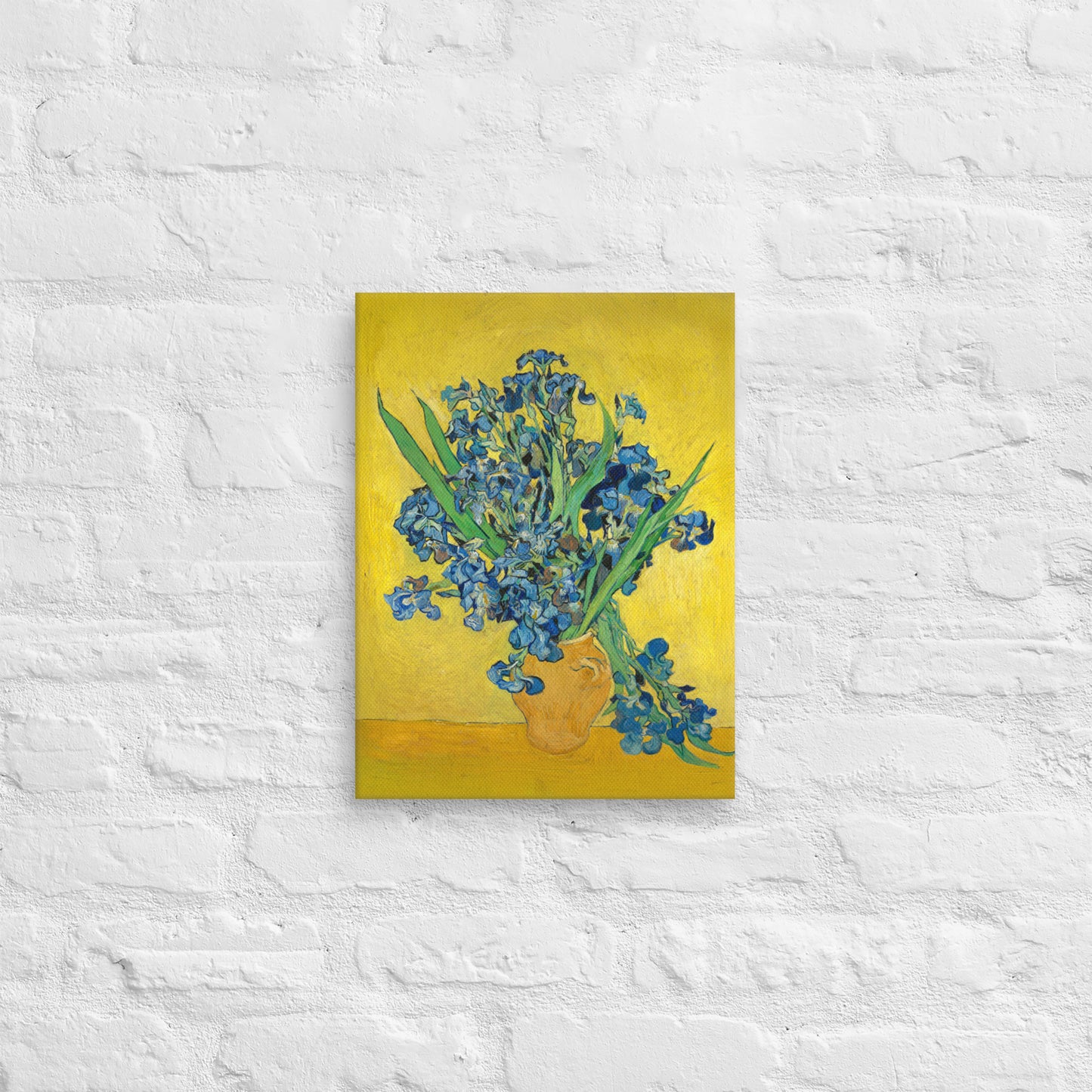 Van Gogh's 'Vase with Irises Against a Yellow Background' on a 12"x16" unframed canvas print on a white brick wall.