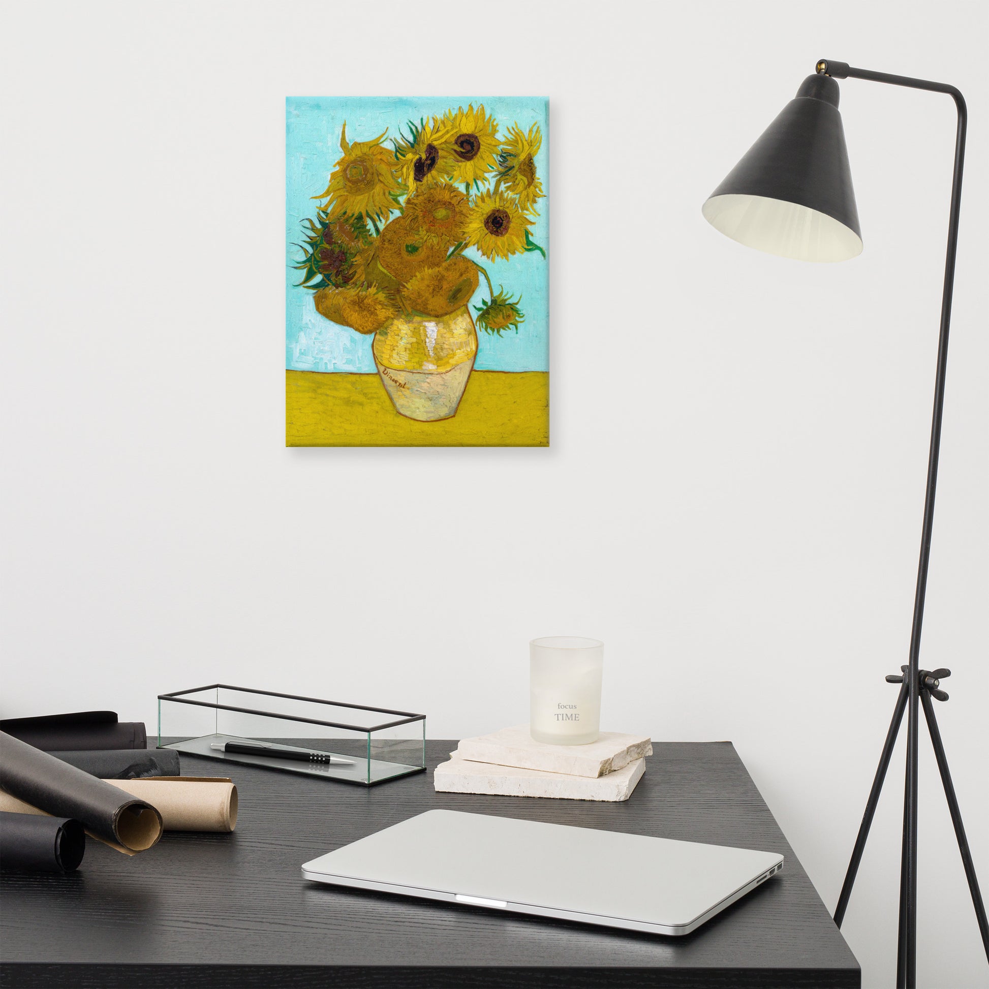 Van Gogh's 'Vase with Twelve Sunflowers' on a 12"x16" unframed canvas print on a white wall above a modern office desk, lamp, and assorted desk items.
