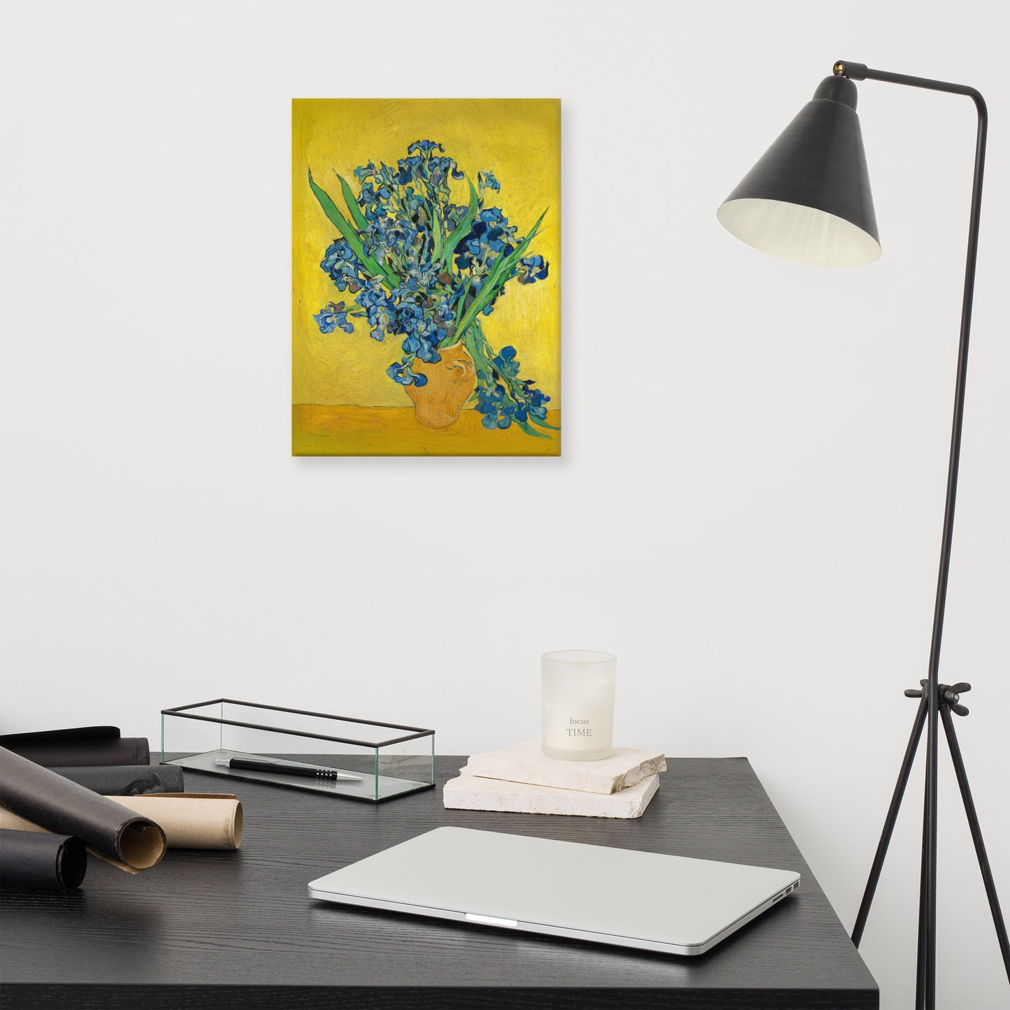 Van Gogh's 'Vase with Irises Against a Yellow Background' on a 12"x16" unframed canvas print on a white wall above a modern office desk, lamp, and assorted desk items.