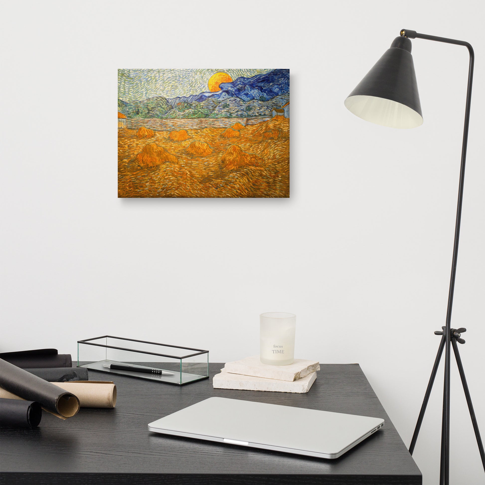 Van Gogh's 'Landscape with Wheat Sheaves and Rising Moon' on a 12"x16" unframed canvas print on a white wall above a modern office desk, lamp, and assorted desk items.