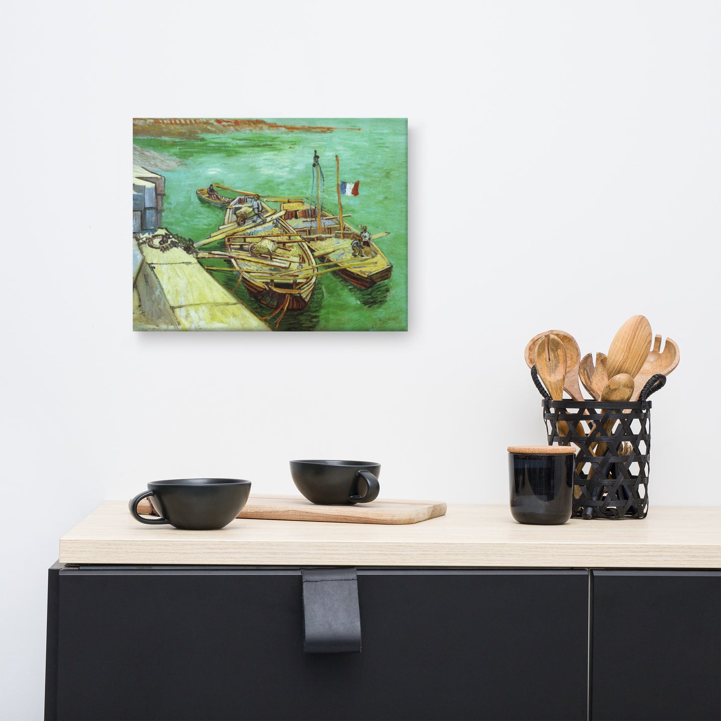 Van Gogh's 'Quay with Men Unloading Sand Barges' on a 12"x16" unframed canvas print on a white wall above a modern office desk, lamp, and assorted desk items.