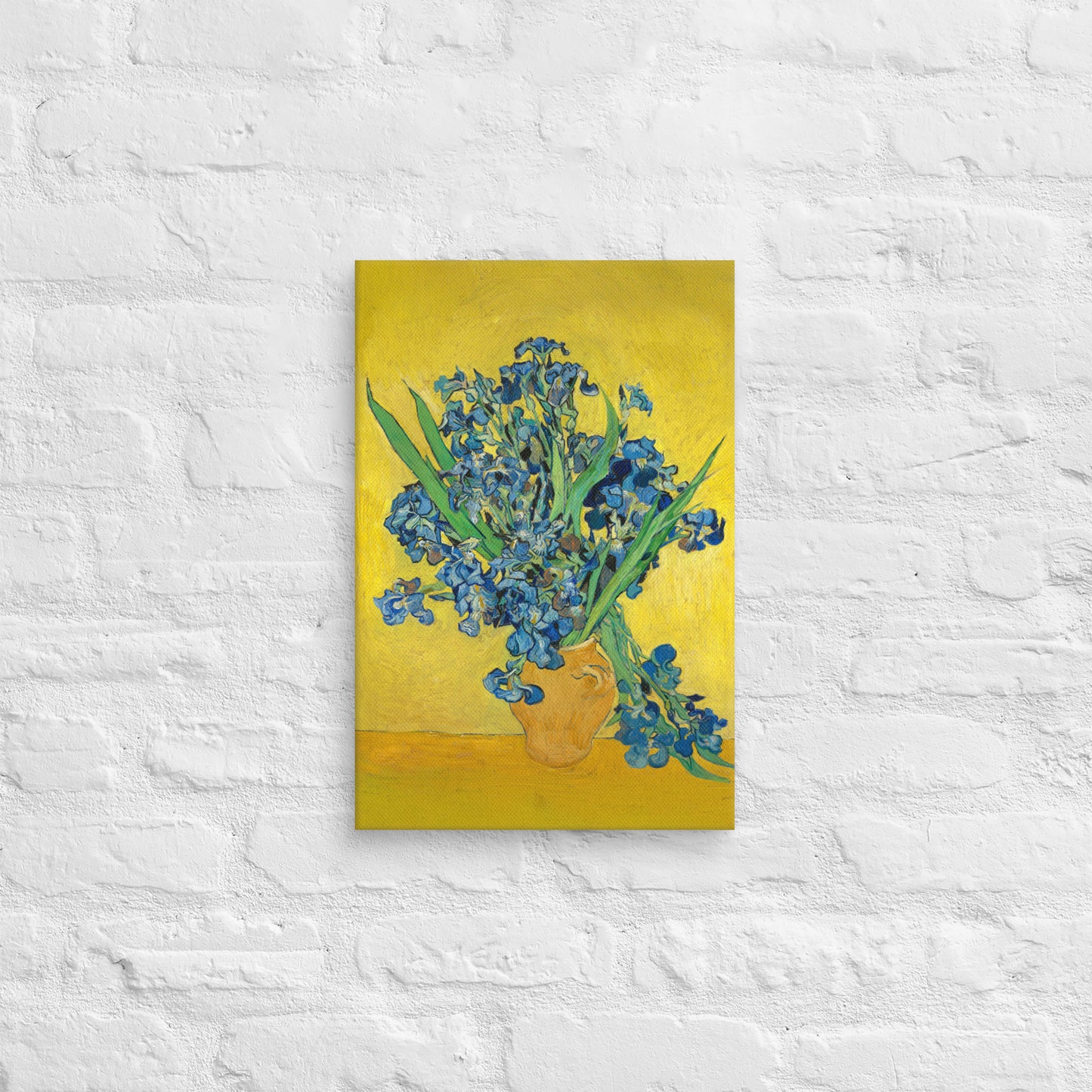Van Gogh's 'Vase with Irises Against a Yellow Background' on a 12"x18" unframed canvas print on a white brick wall.