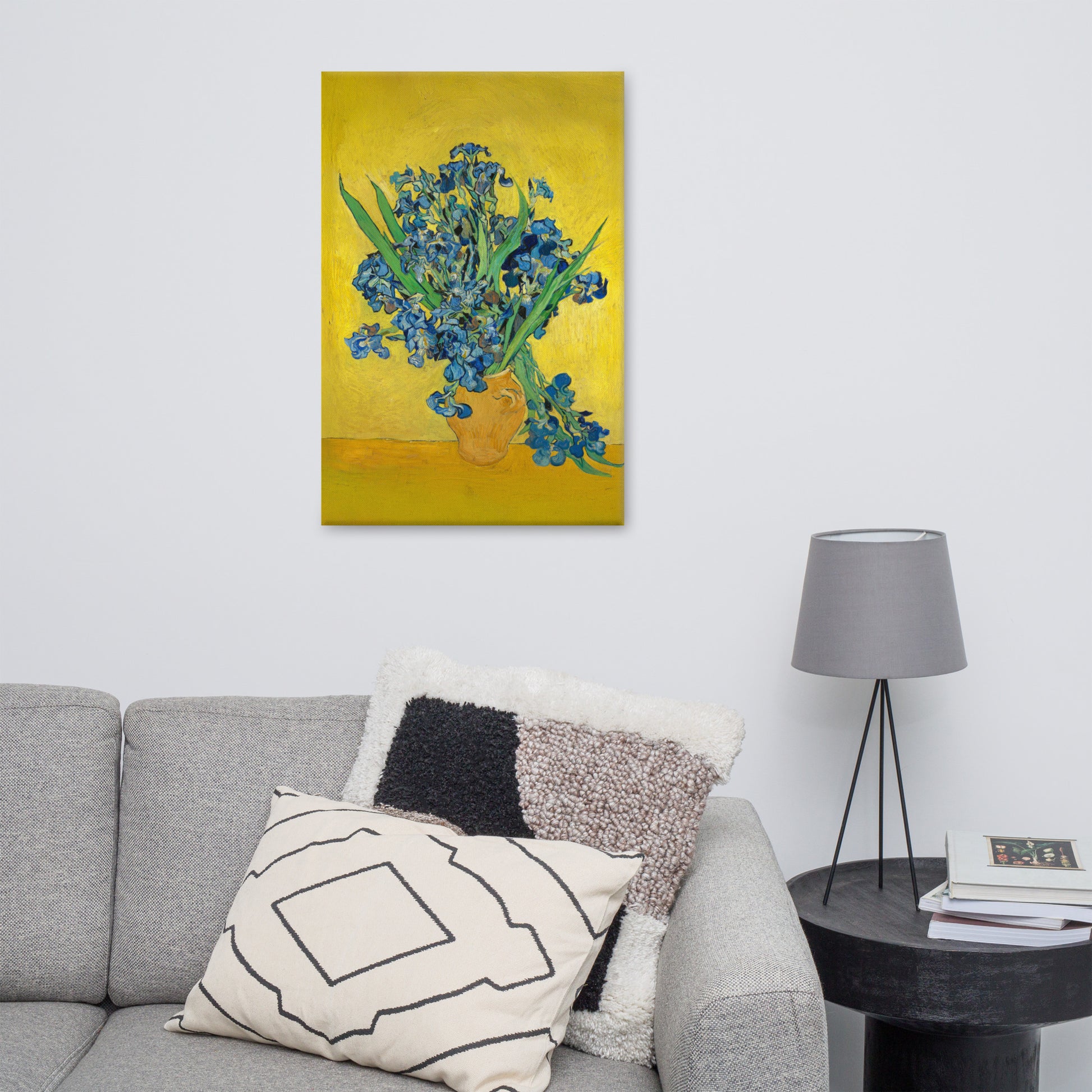 Van Gogh's 'Vase with Irises Against a Yellow Background' on a 24"x36" unframed canvas print on a white wall above a gray sofa with throw pillows and side table with a lamp.