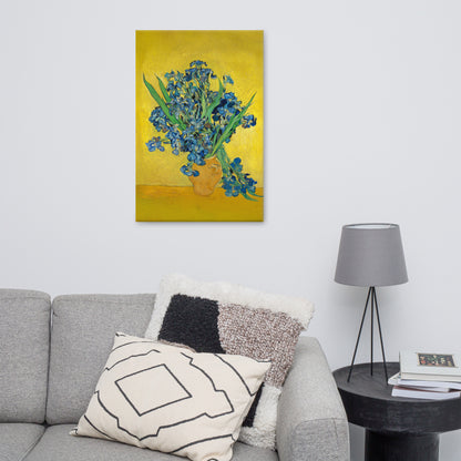 Van Gogh's 'Vase with Irises Against a Yellow Background' on a 24"x36" unframed canvas print on a white wall above a gray sofa with throw pillows and side table with a lamp.