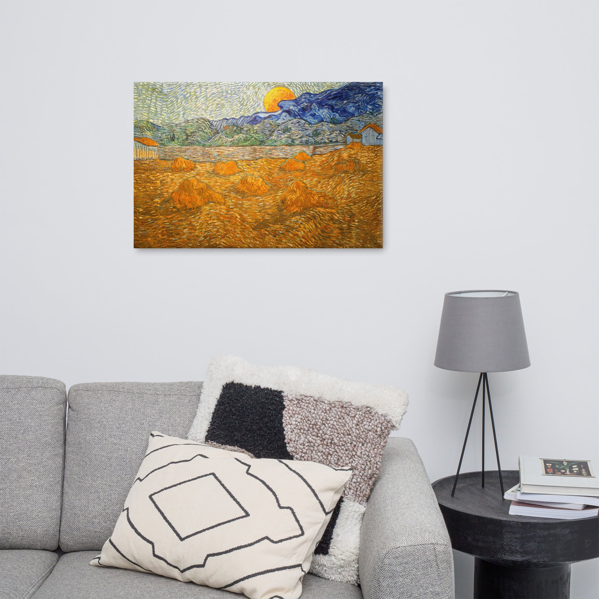 Van Gogh's 'Landscape with Wheat Sheaves and Rising Moon' on a 24"x36" unframed canvas print on a white wall above a gray sofa with throw pillows and side table with a lamp.