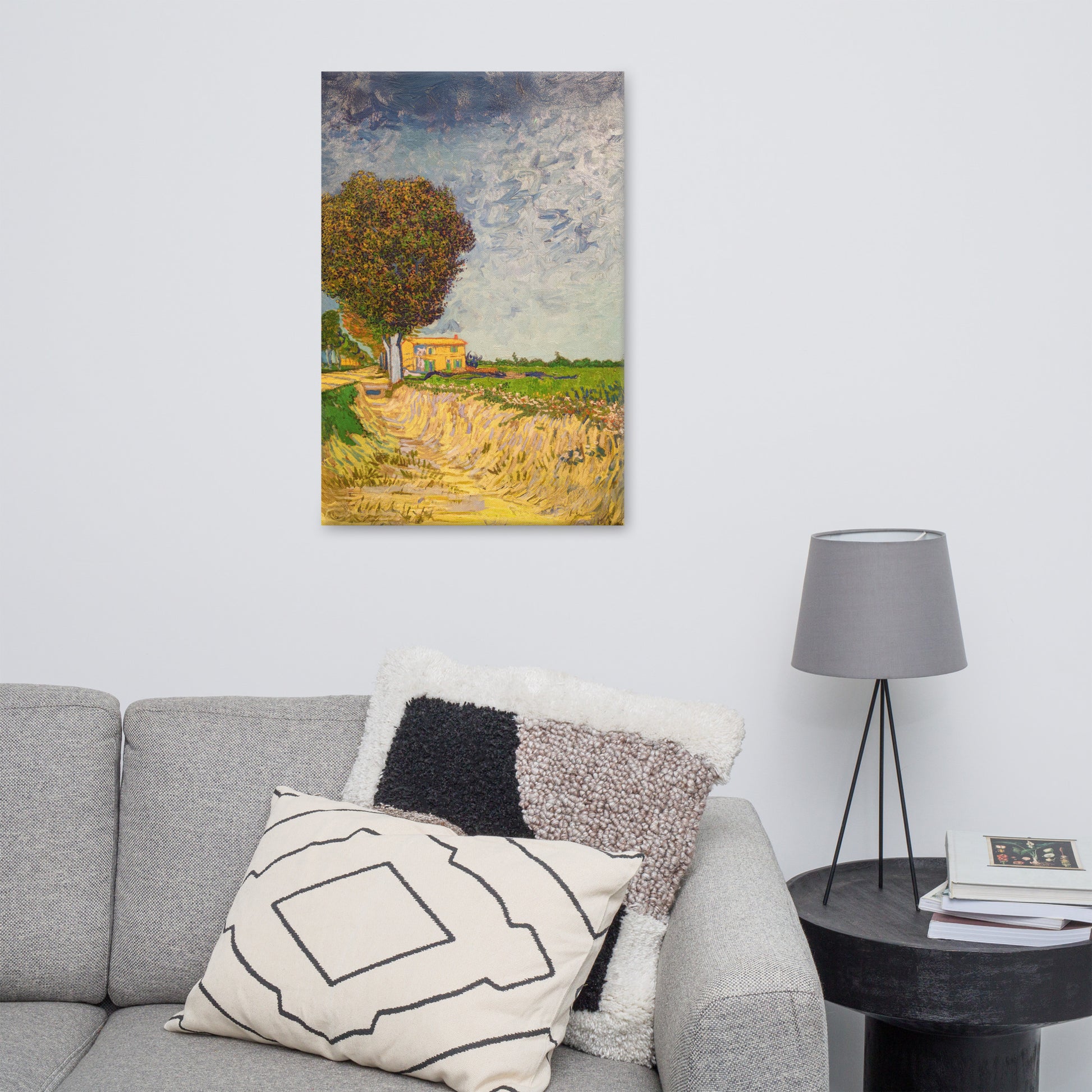 Van Gogh's 'A Lane near Arles' on a 24"x36" unframed canvas print on a white wall above a gray sofa with throw pillows and side table with a lamp.