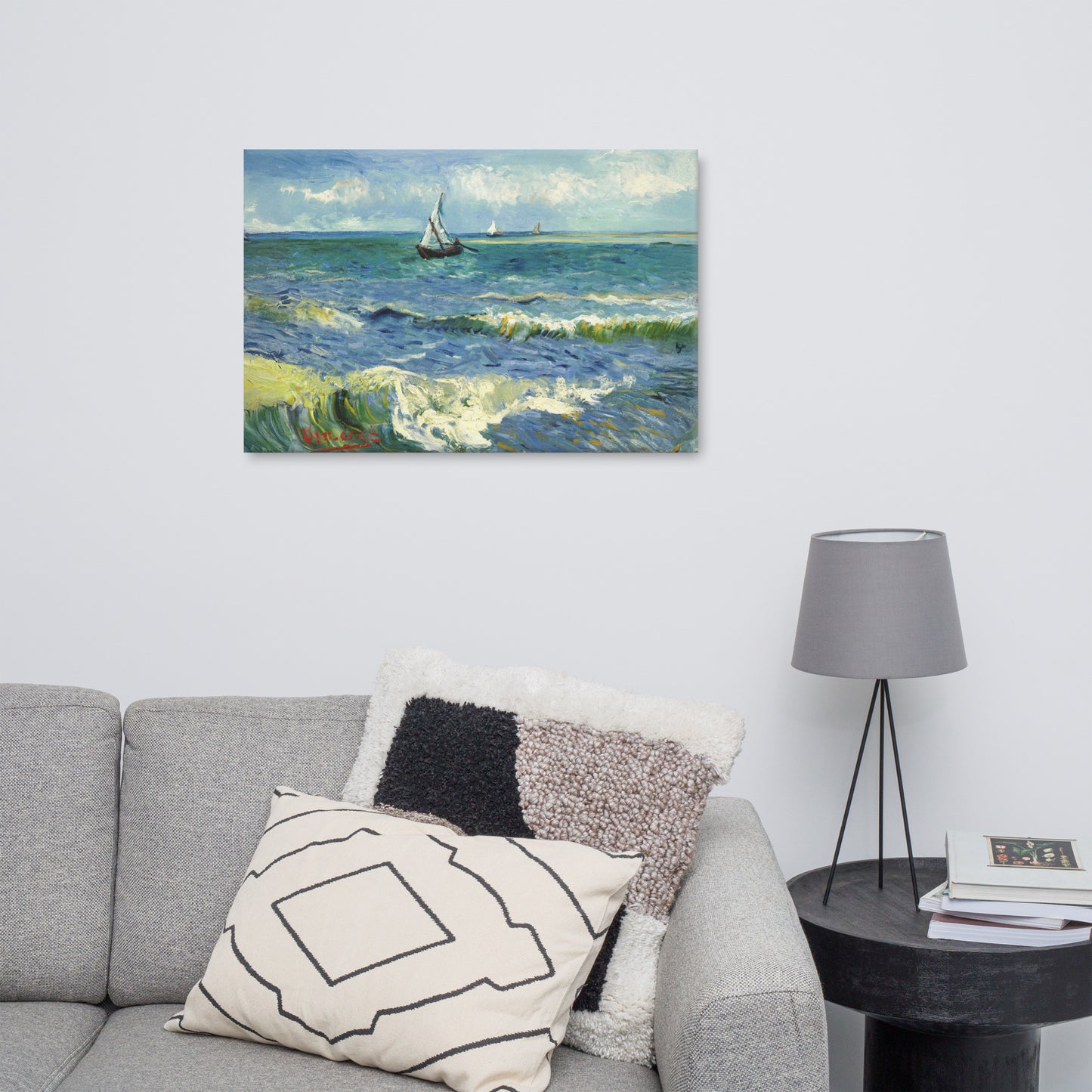 Van Gogh's 'The Sea at Les Saintes-Maries-de-la-Mer' on a 24"x36" unframed canvas print on a white wall above a gray sofa with throw pillows and side table with a lamp.