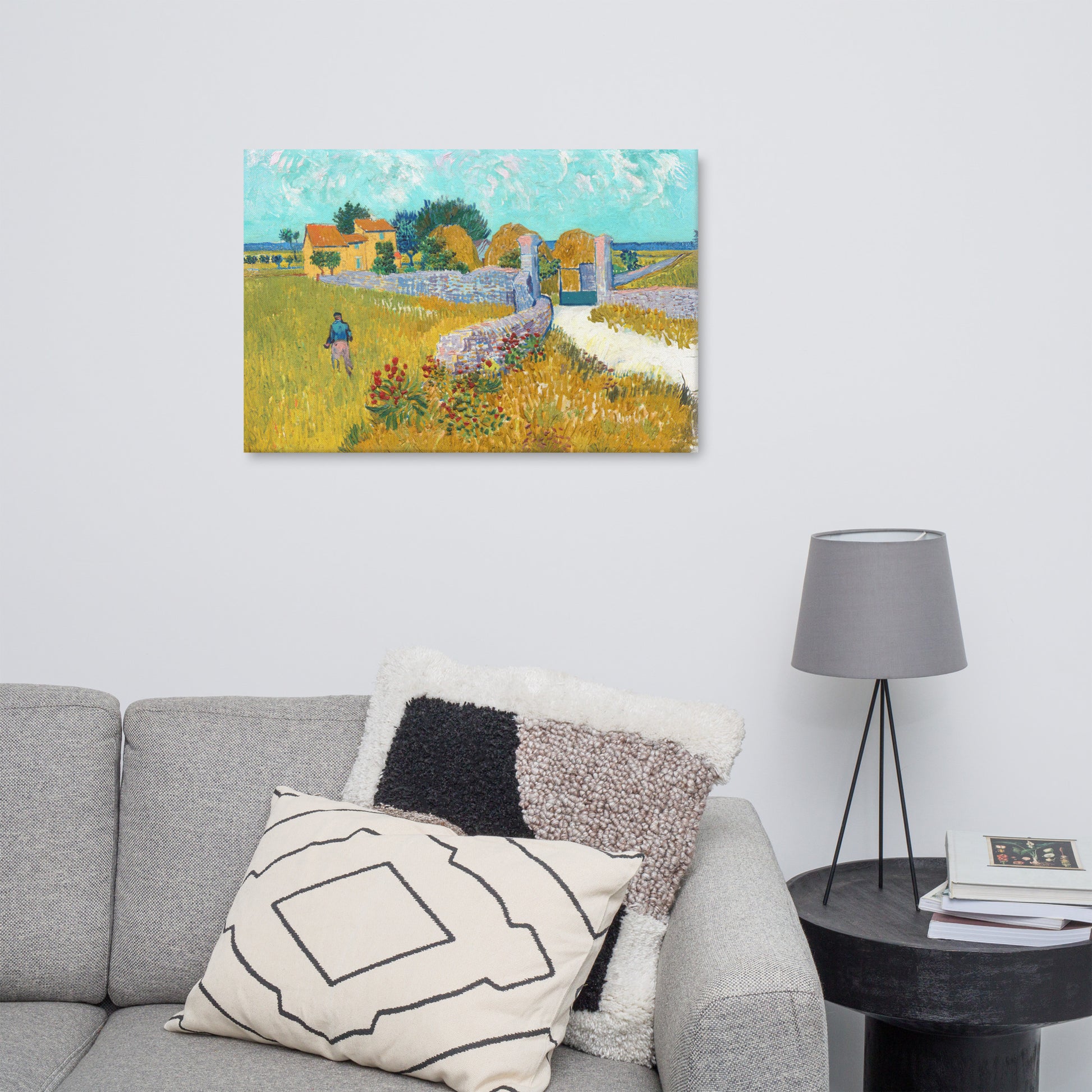 Van Gogh's 'Farmhouse in Provence' on a 24"x36" unframed canvas print on a white wall above a gray sofa with throw pillows and side table with a lamp.
