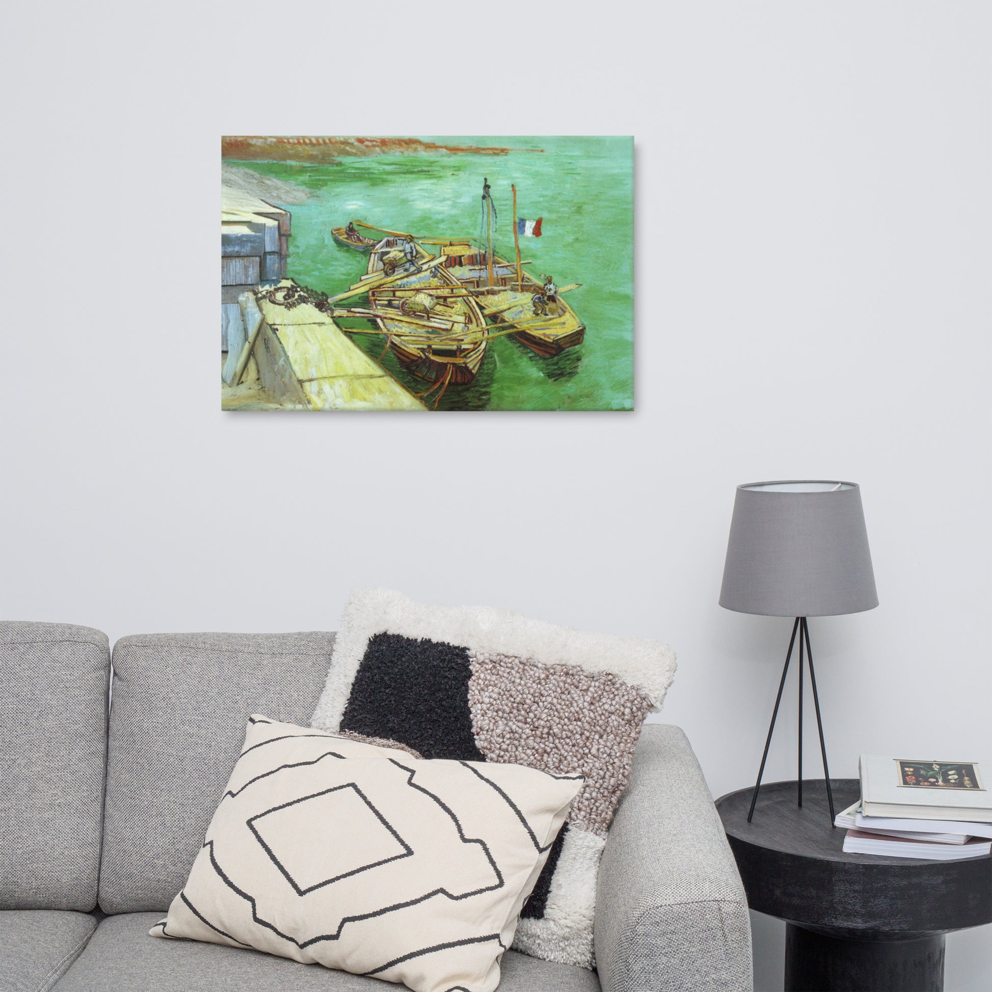 Van Gogh's 'Quay with Men Unloading Sand Barges' on a 24"x36" unframed canvas print on a white wall above a gray sofa with throw pillows and side table with a lamp.