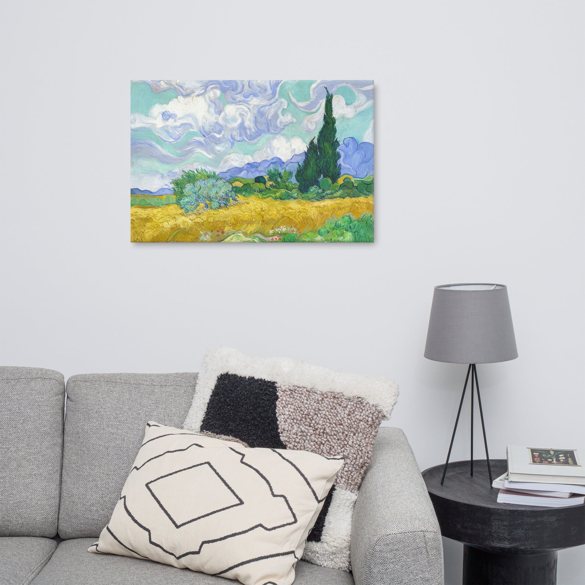 Van Gogh's 'Wheat Field with Cypresses' on a 24"x36" unframed canvas print on a white wall above a gray sofa with throw pillows and side table with a lamp.