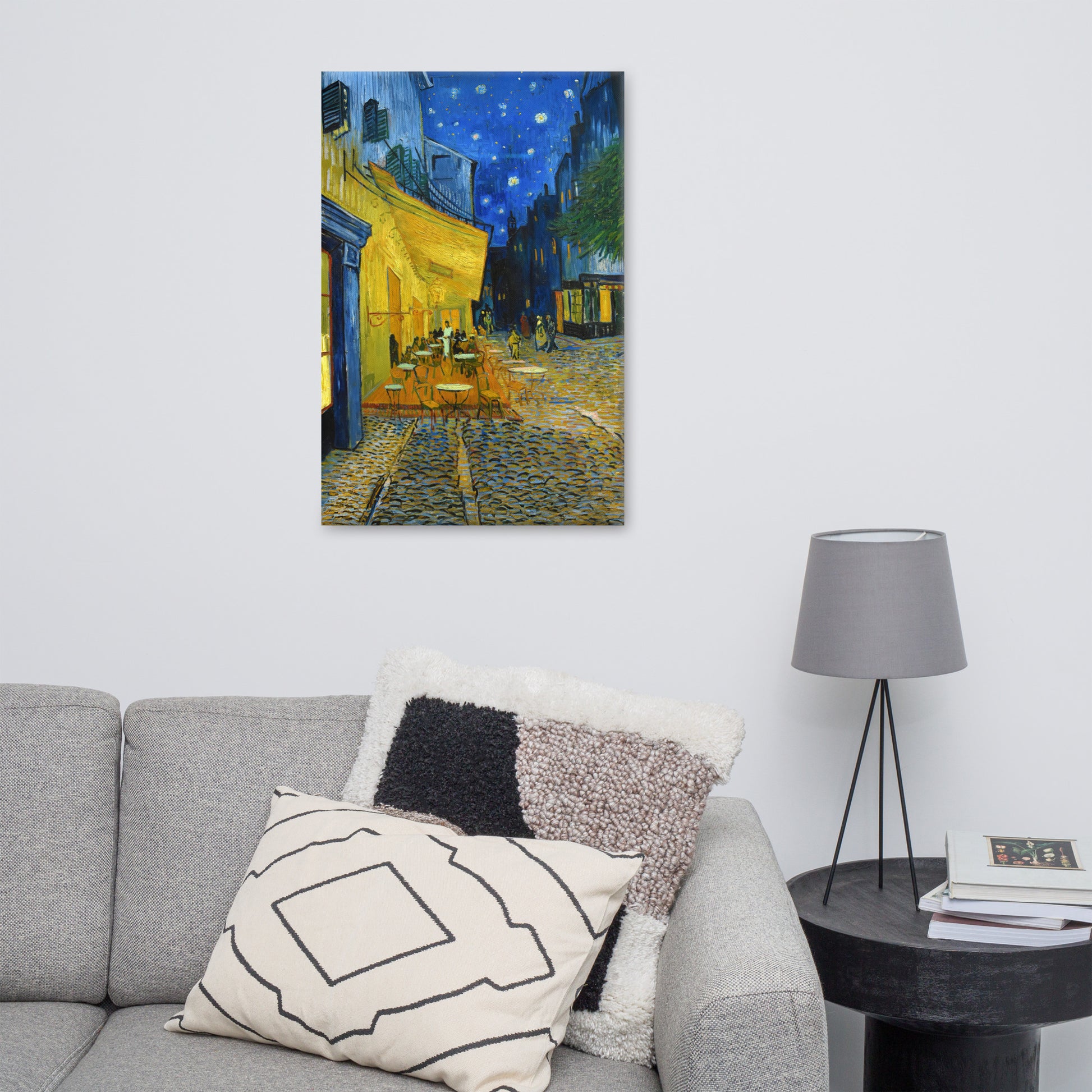 Van Gogh's 'Café Terrace at Night' on a 24"x36" unframed canvas print on a white wall above a gray sofa with throw pillows and side table with a lamp.
