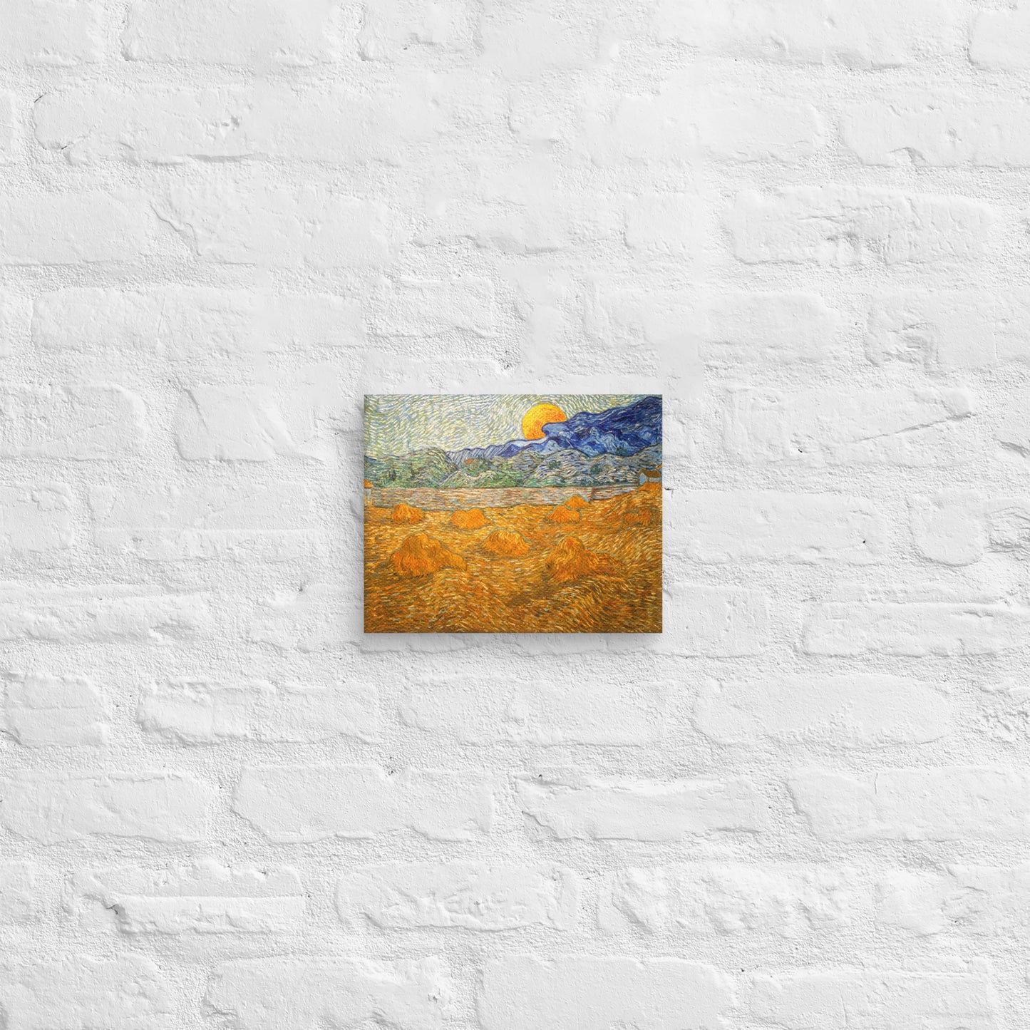 Van Gogh's 'Landscape with Wheat Sheaves and Rising Moon' on a 8"x10" unframed canvas print on a white brick wall.
