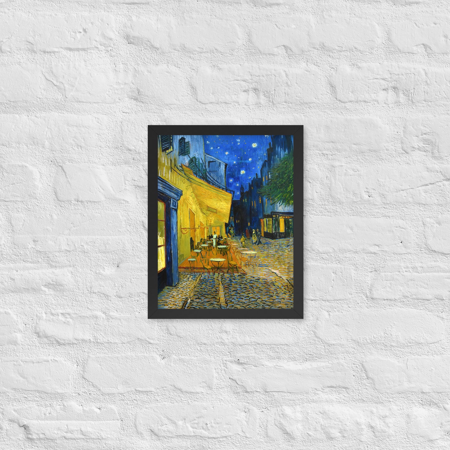 Van Gogh's 'Café Terrace at Night' on a 11"x14" black framed poster print on a white brick wall.