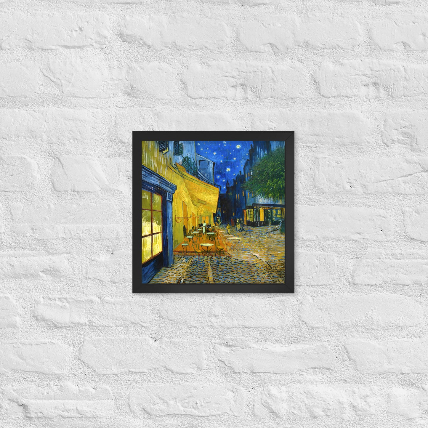 Van Gogh's 'Café Terrace at Night' on a 12"x12" black framed poster print on a white brick wall.