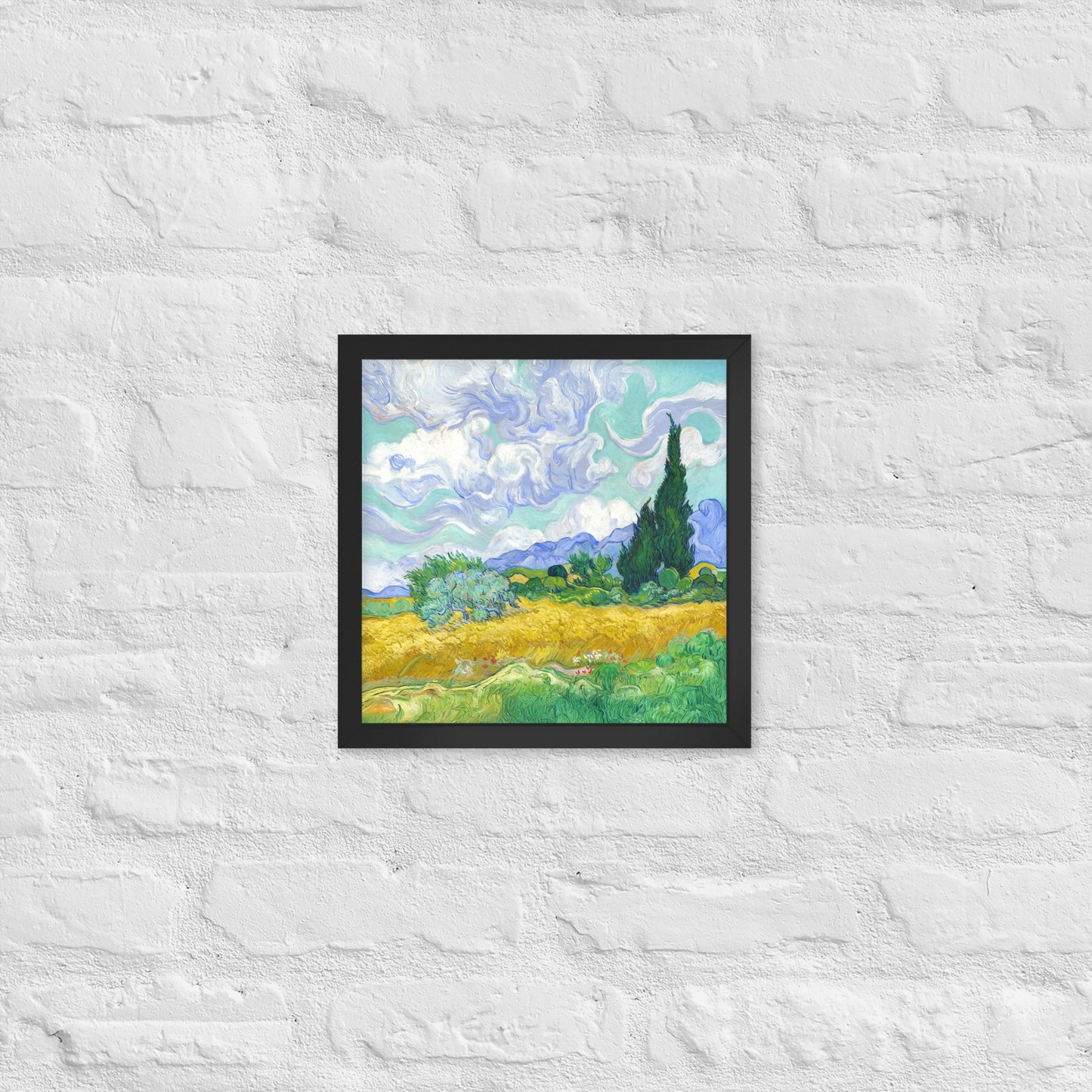 Van Gogh's 'Wheat Field with Cypresses' on a 12"x12" black framed poster print on a white brick wall.