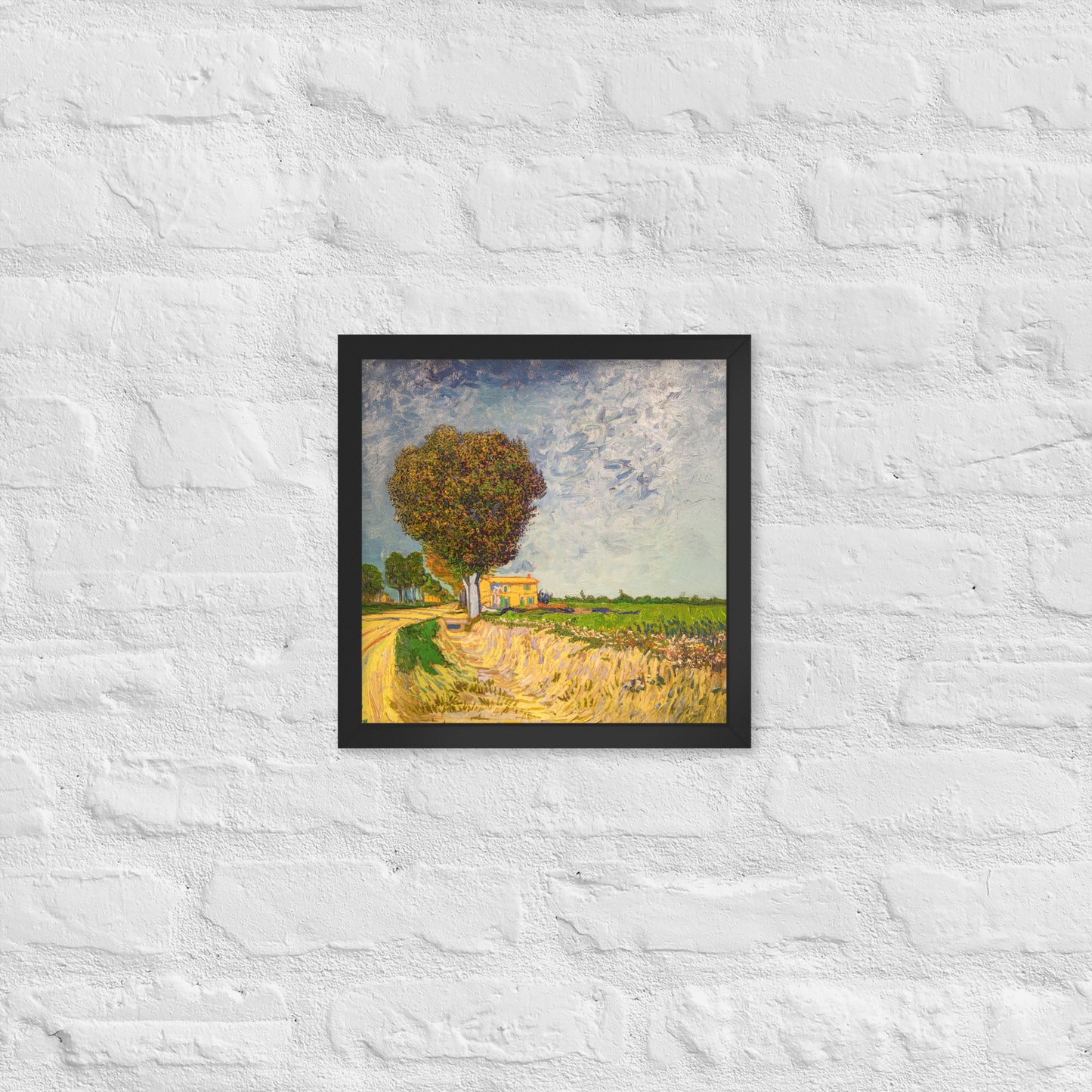 Van Gogh's 'A Lane near Arles' on a 12"x12" black framed poster print on a white brick wall.