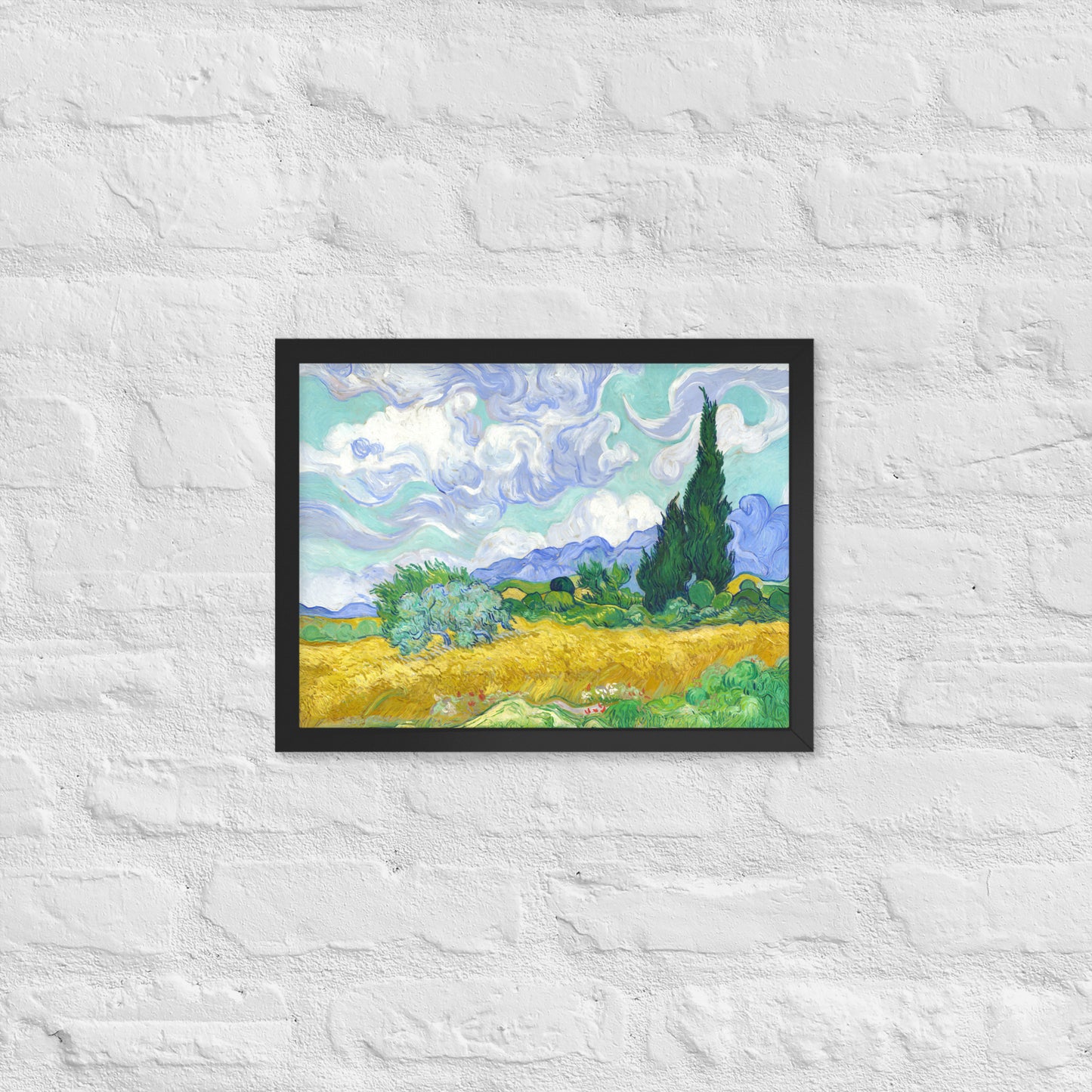 Van Gogh's 'Wheat Field with Cypresses' on a 12"x16" black framed poster print on a white brick wall.