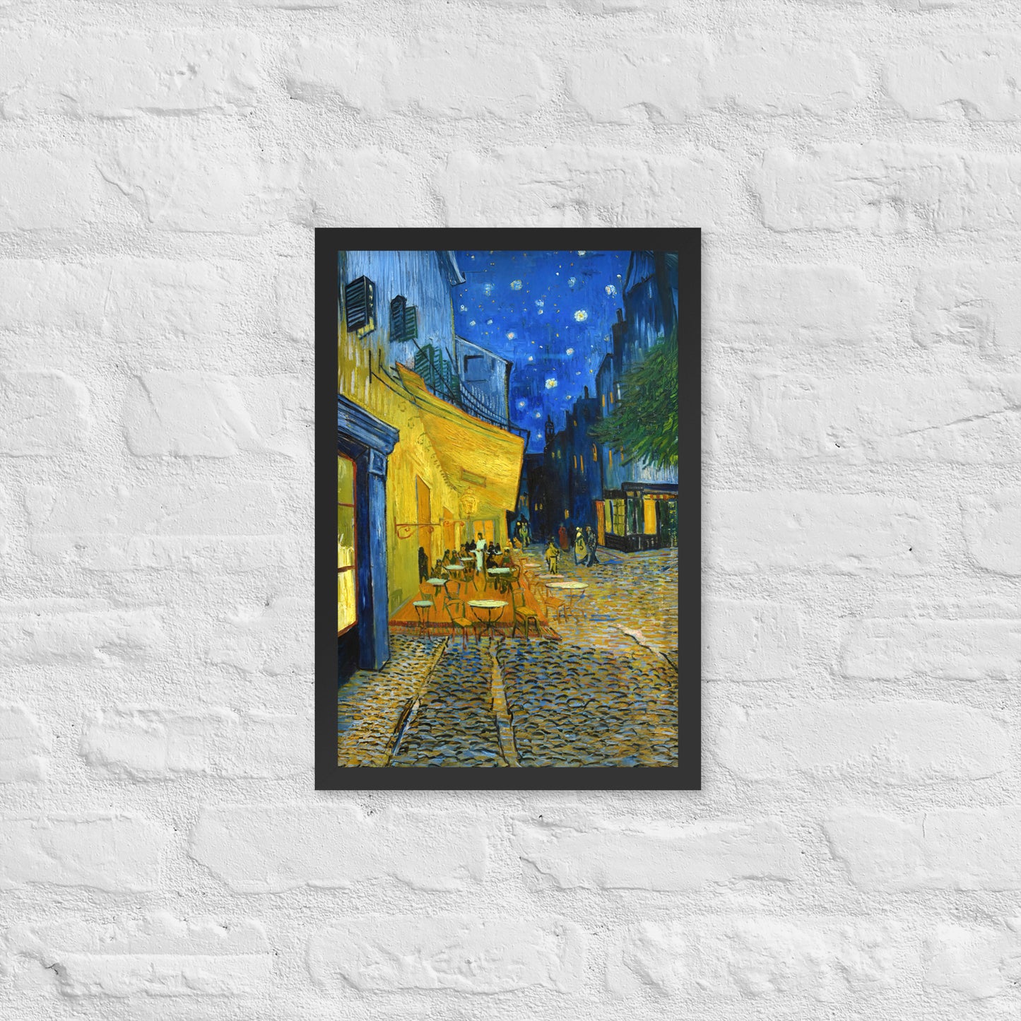 Van Gogh's 'Café Terrace at Night' on a 12"x18" black framed poster print on a white brick wall.