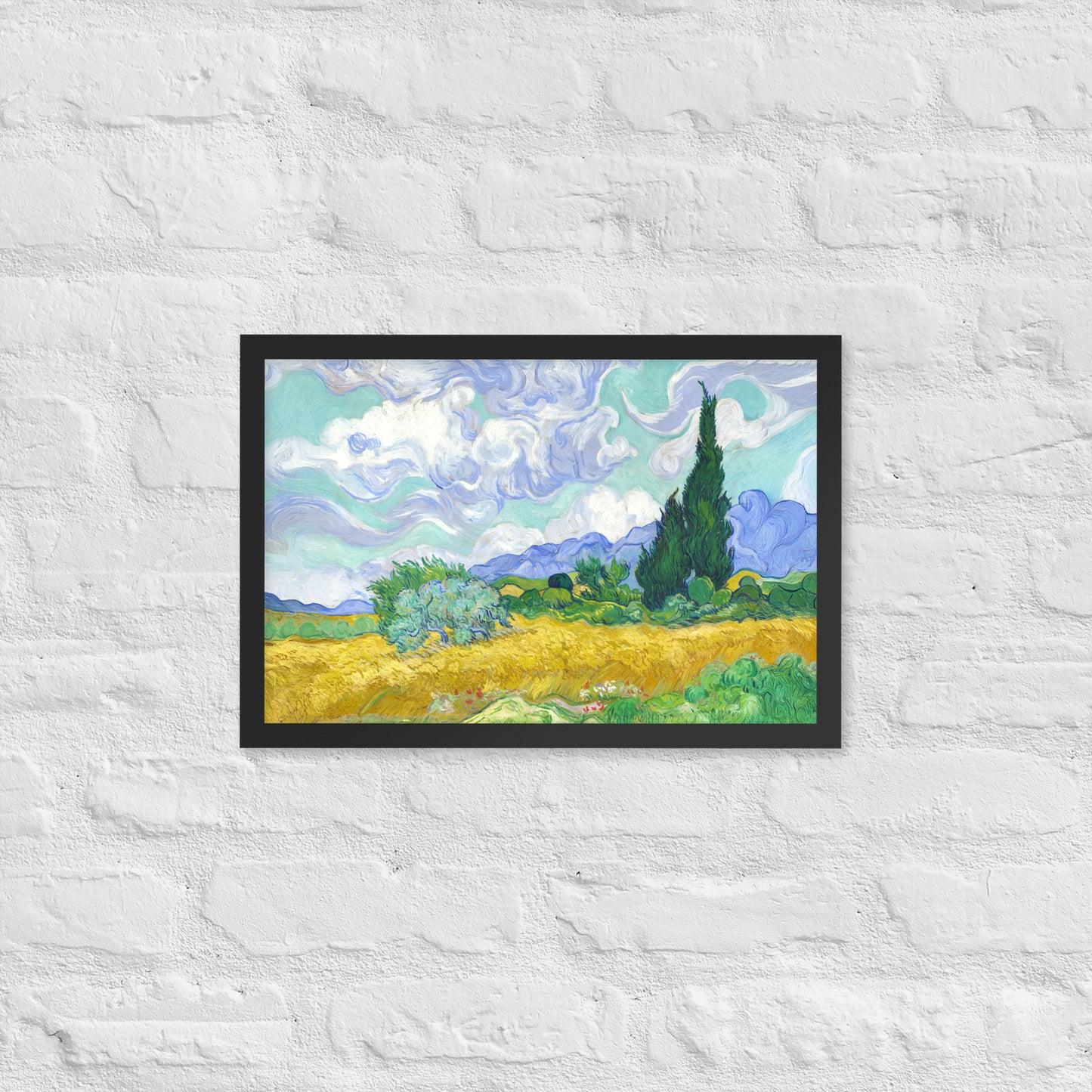 Van Gogh's 'Wheat Field with Cypresses' on a 12"x18" black framed poster print on a white brick wall.