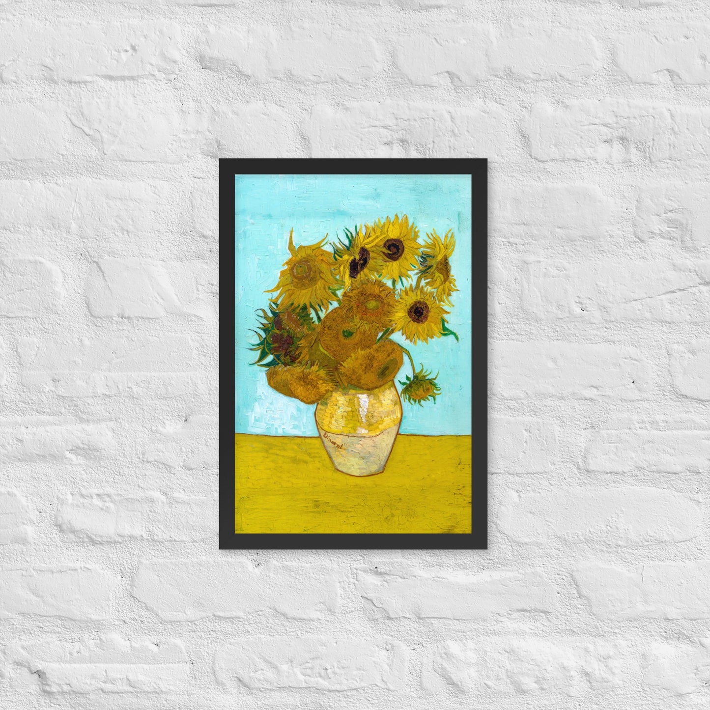 Van Gogh's 'Vase with Twelve Sunflowers' on a 12"x18" black framed poster print on a white brick wall.