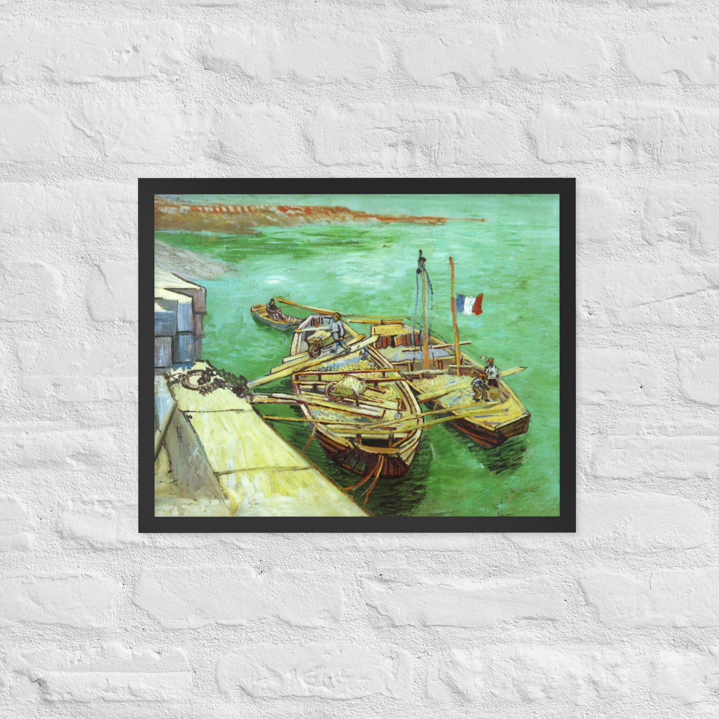 Van Gogh's 'Quay with Men Unloading Sand Barges' on a 16"x20" black framed poster print on a white brick wall.
