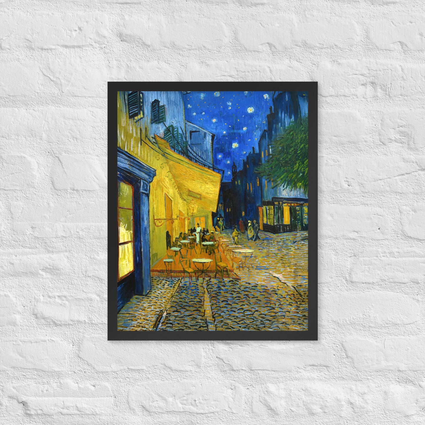 Van Gogh's 'Café Terrace at Night' on a 16"x20" black framed poster print on a white brick wall.