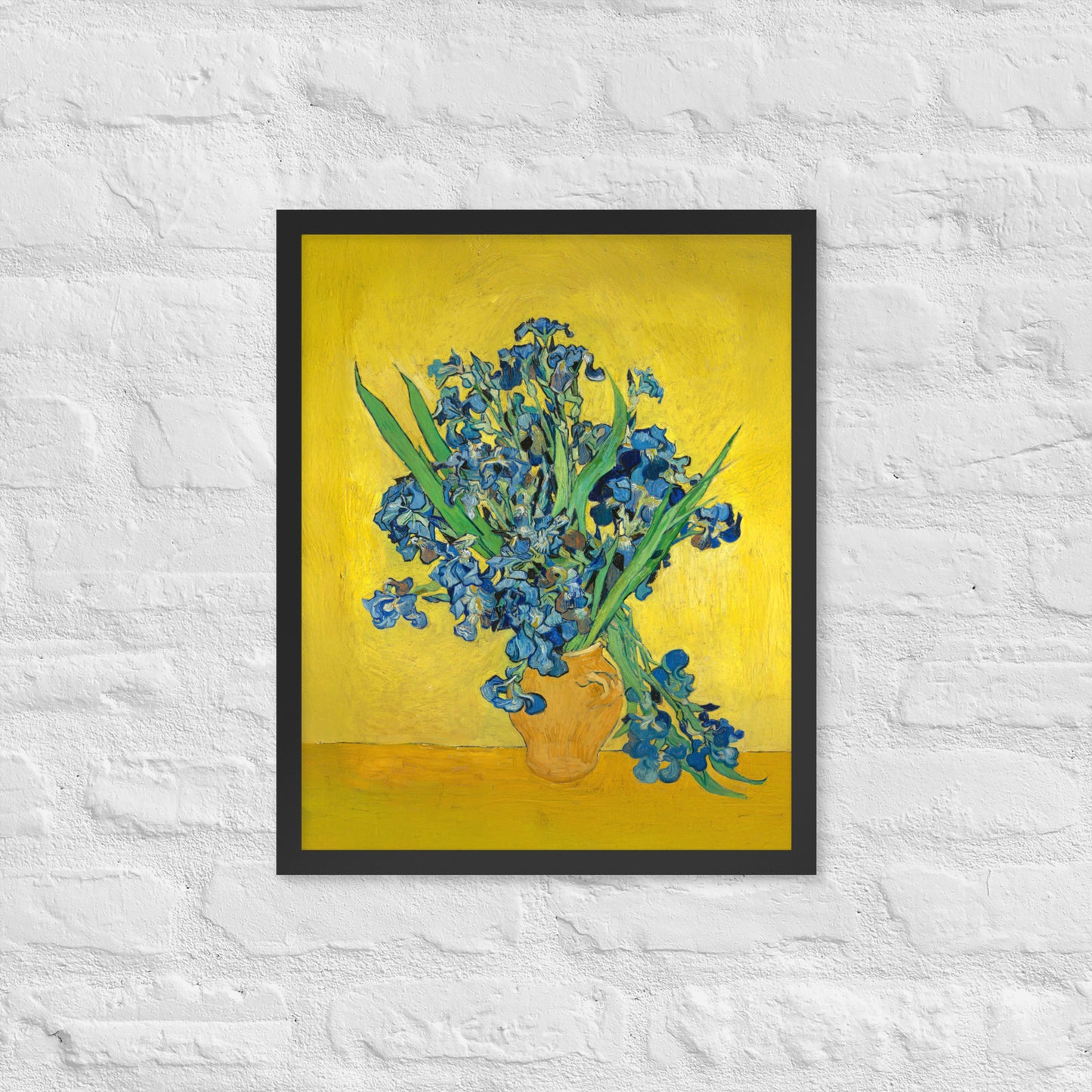 Van Gogh's 'Vase with Irises Against a Yellow Background' on a 16"x20" black framed poster print on a white brick wall.
