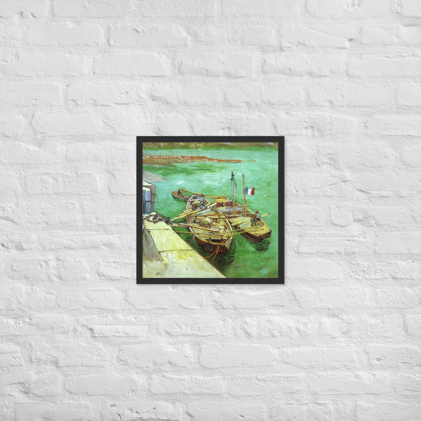Van Gogh's 'Quay with Men Unloading Sand Barges' on a 18"x18" black framed poster print on a white brick wall.