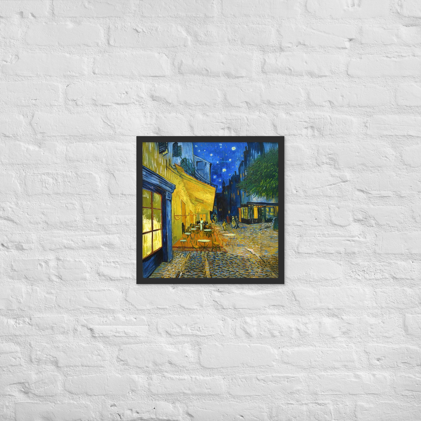 Van Gogh's 'Café Terrace at Night' on a 18"x18" black framed poster print on a white brick wall.