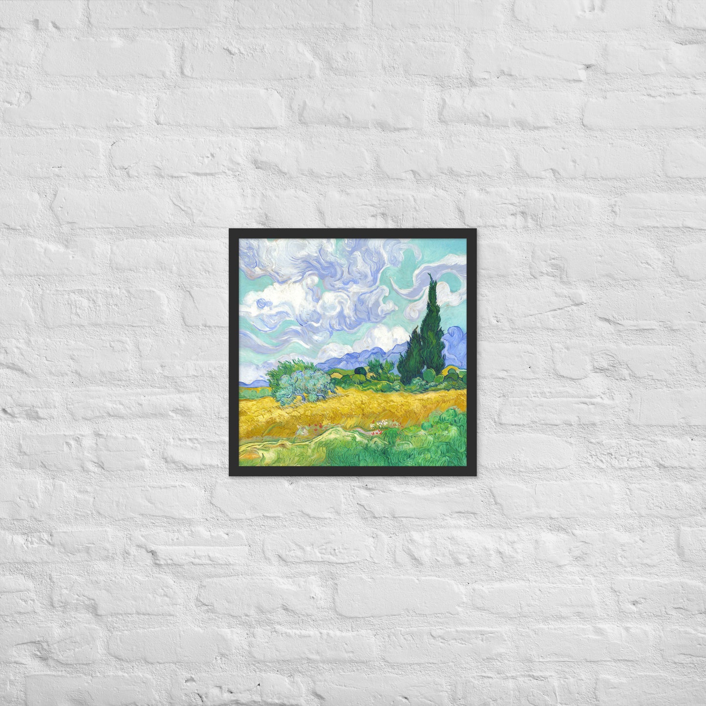Van Gogh's 'Wheat Field with Cypresses' on a 18"x18" black framed poster print on a white brick wall.