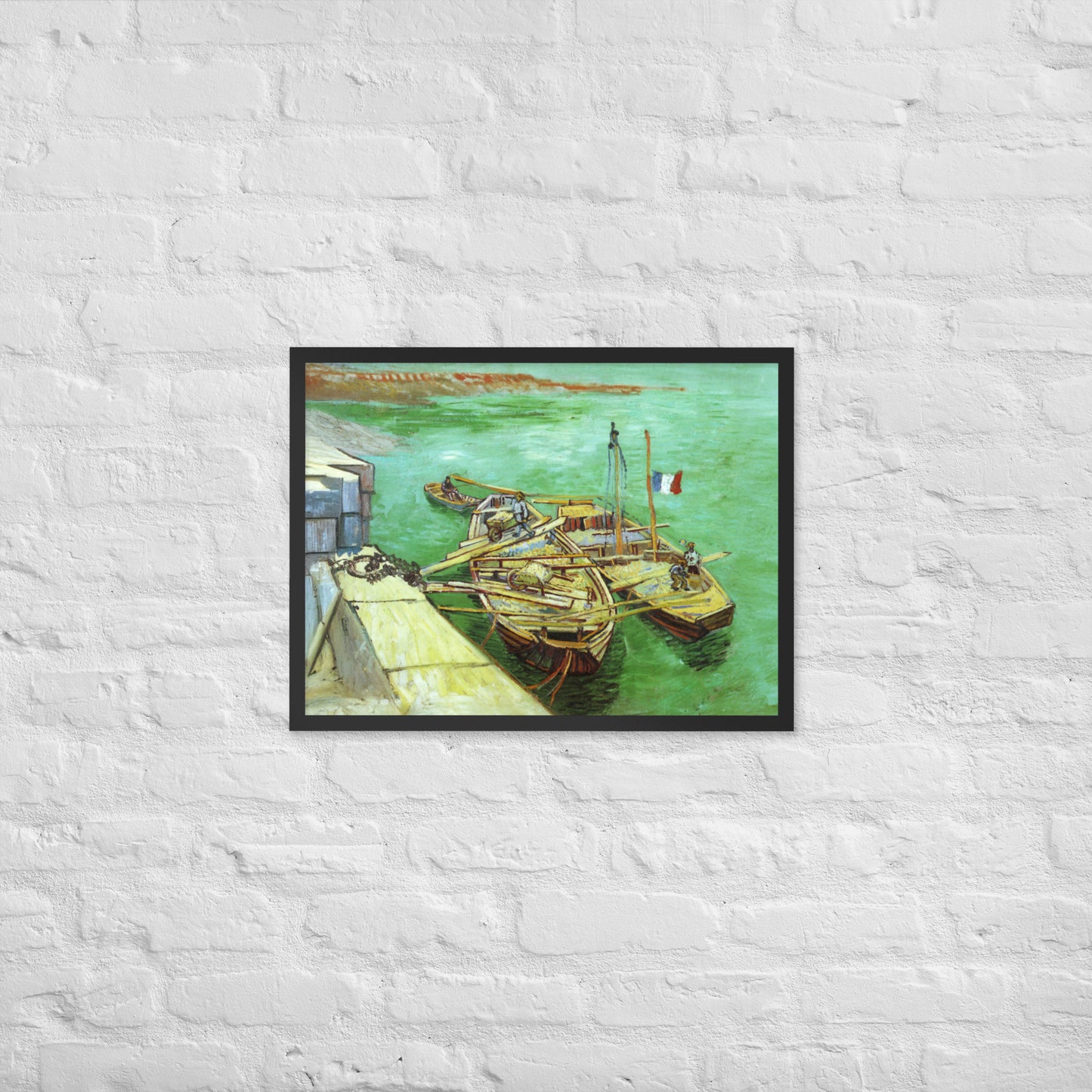 Van Gogh's 'Quay with Men Unloading Sand Barges' on a 18"x24" black framed poster print on a white brick wall.