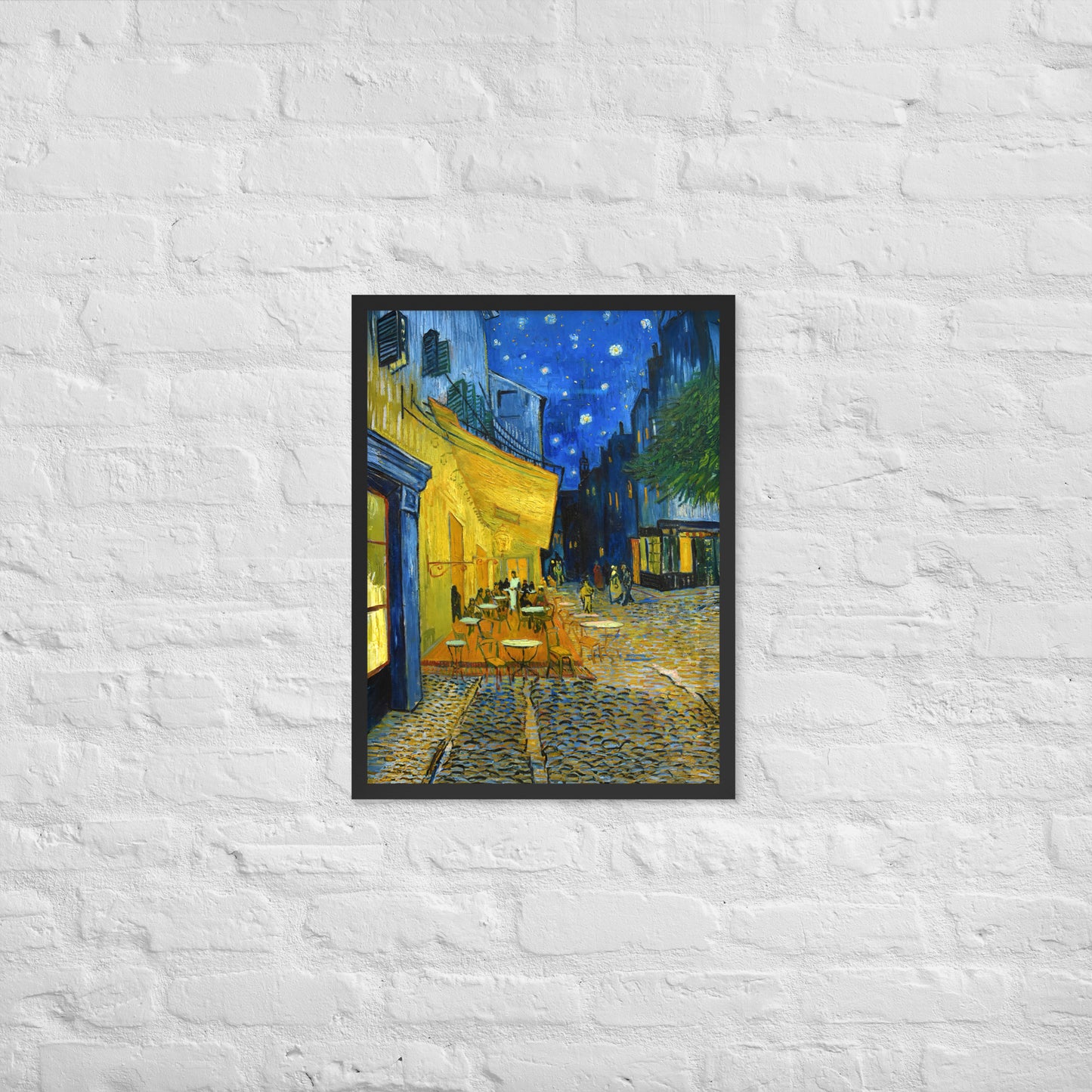 Van Gogh's 'Café Terrace at Night' on a 18"x24" black framed poster print on a white brick wall.