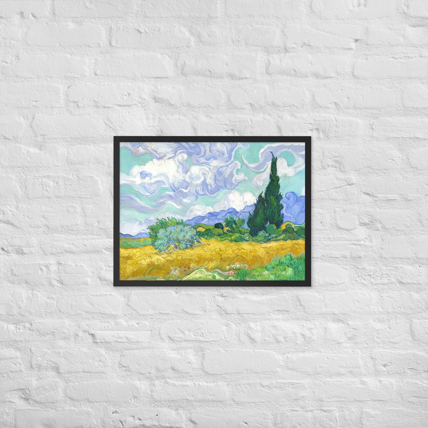 Van Gogh's 'Wheat Field with Cypresses' on a 18"x24" black framed poster print on a white brick wall.