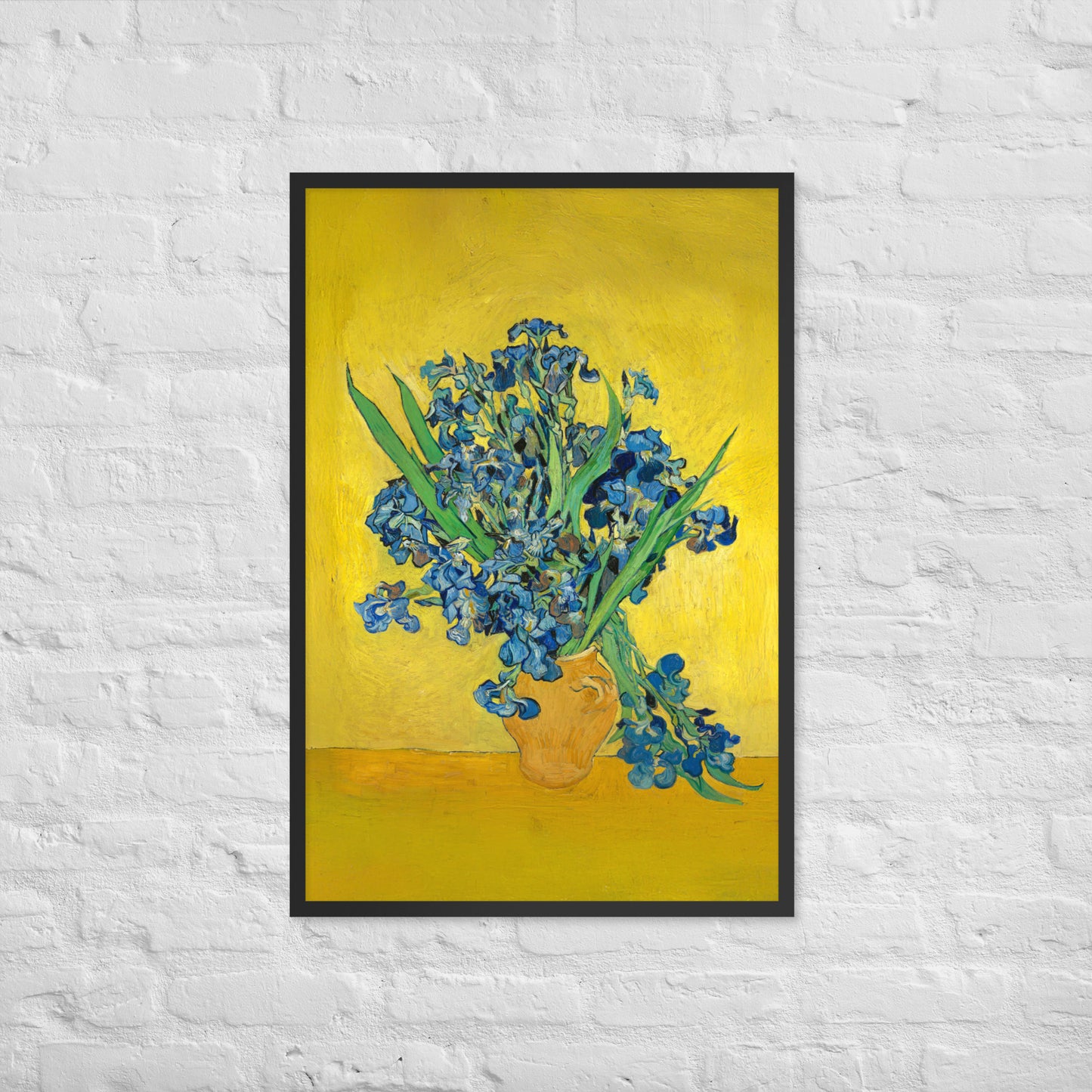 Van Gogh's 'Vase with Irises Against a Yellow Background' on a 24"x36" black framed poster print on a white brick wall.