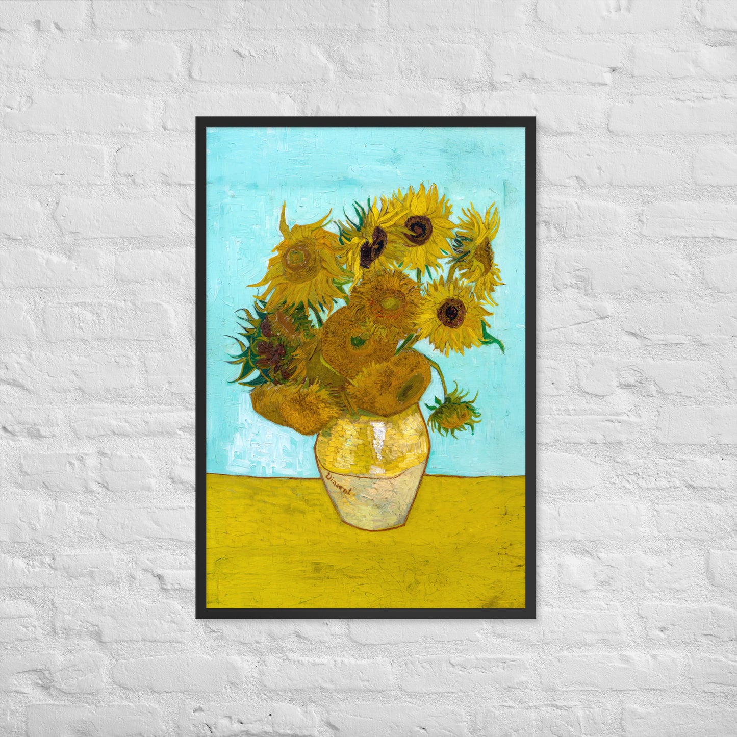 Van Gogh's 'Vase with Twelve Sunflowers' on a 24"x36" black framed poster print on a white brick wall.