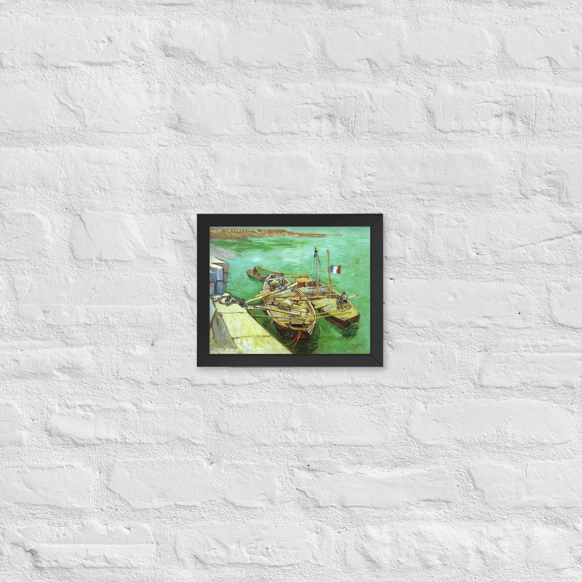 Van Gogh's 'Quay with Men Unloading Sand Barges' on a 8"x10" black framed poster print on a white brick wall.