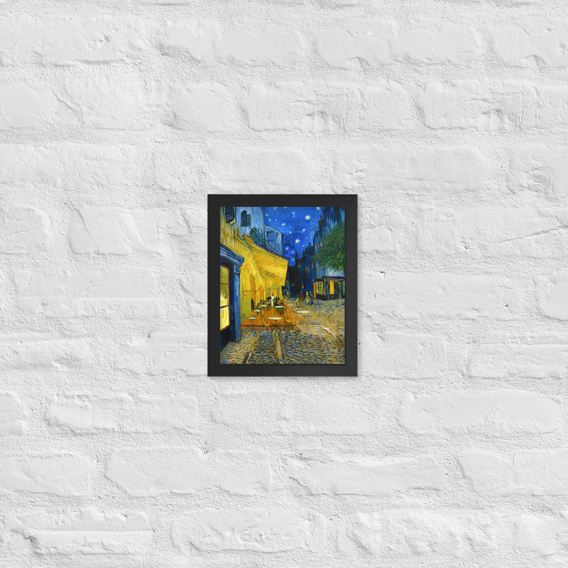 Van Gogh's 'Café Terrace at Night' on a 8"x10" black framed poster print on a white brick wall.