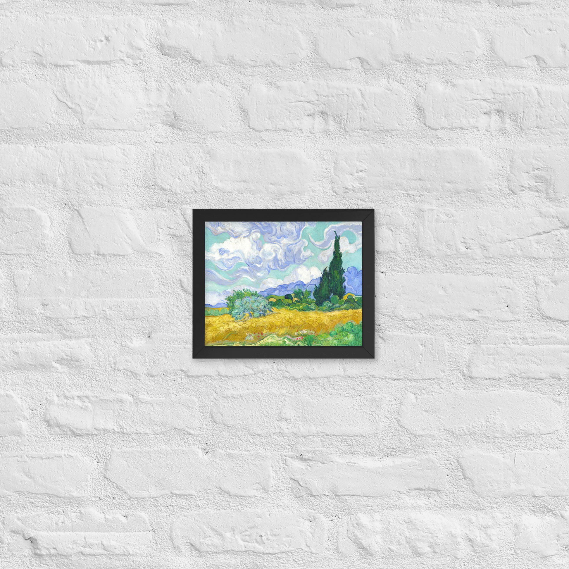 Van Gogh's 'Wheat Field with Cypresses' on a 8"x10" black framed poster print on a white brick wall.