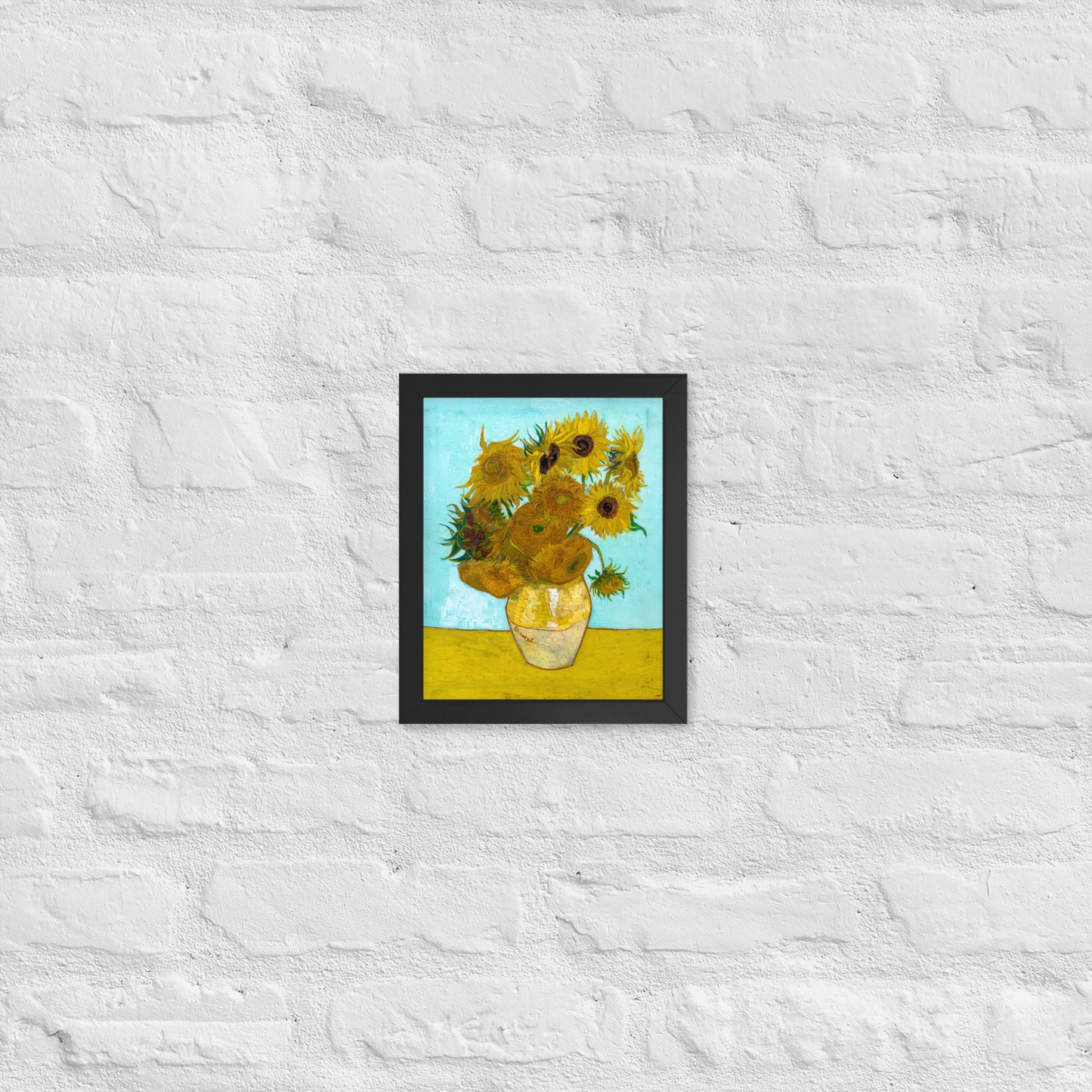 Van Gogh's 'Vase with Twelve Sunflowers' on a 8"x10" black framed poster print on a white brick wall.