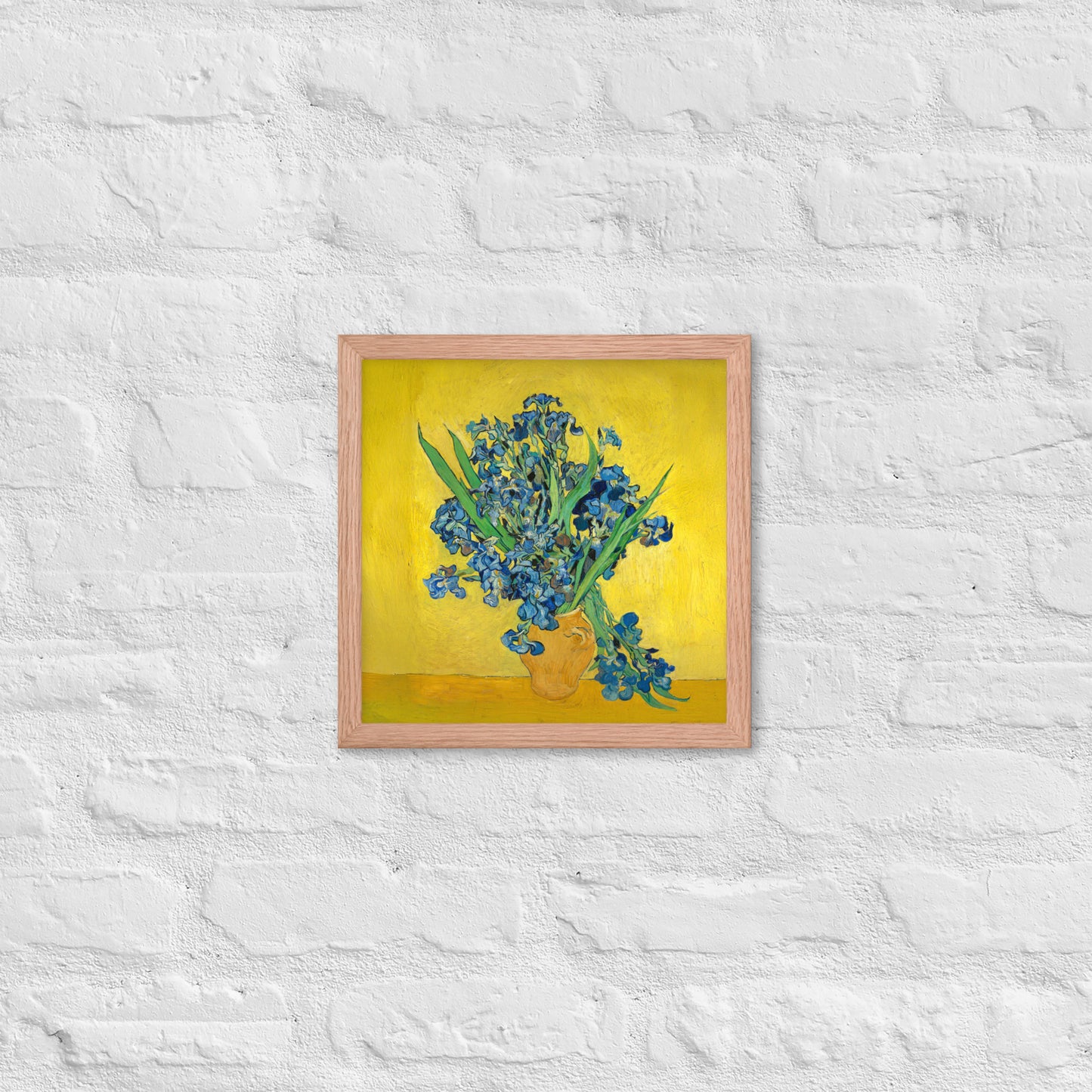 Van Gogh's 'Vase with Irises Against a Yellow Background' on a 12"x12" red oak framed poster print on a white brick wall.