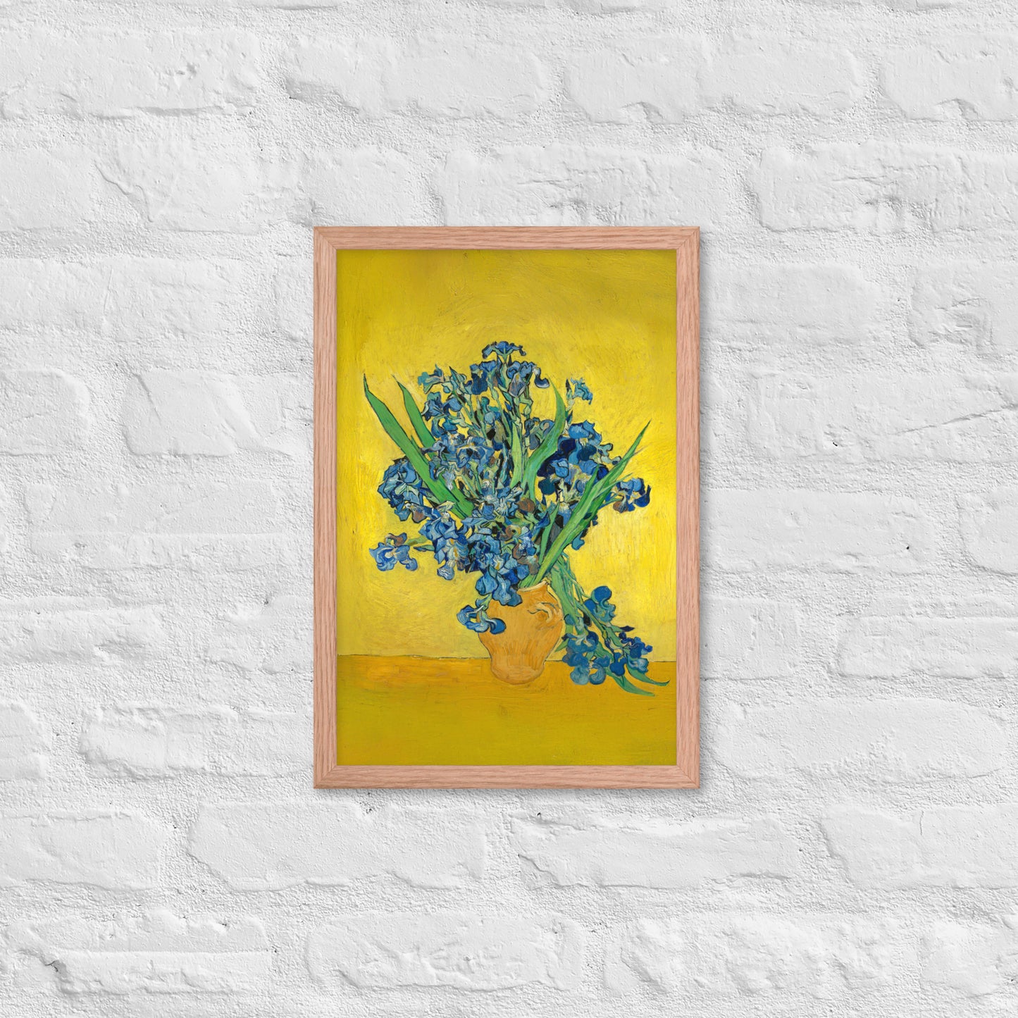 Van Gogh's 'Vase with Irises Against a Yellow Background' on a 12"x18" red oak framed poster print on a white brick wall.