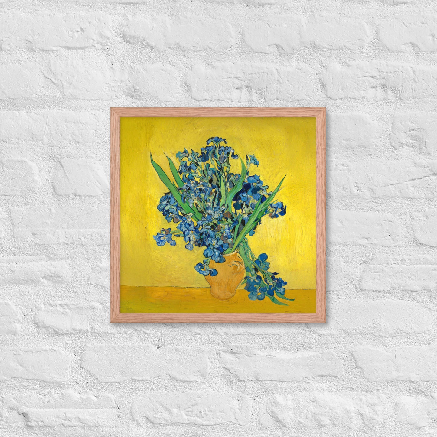 Van Gogh's 'Vase with Irises Against a Yellow Background' on a 16"x16" red oak framed poster print on a white brick wall.