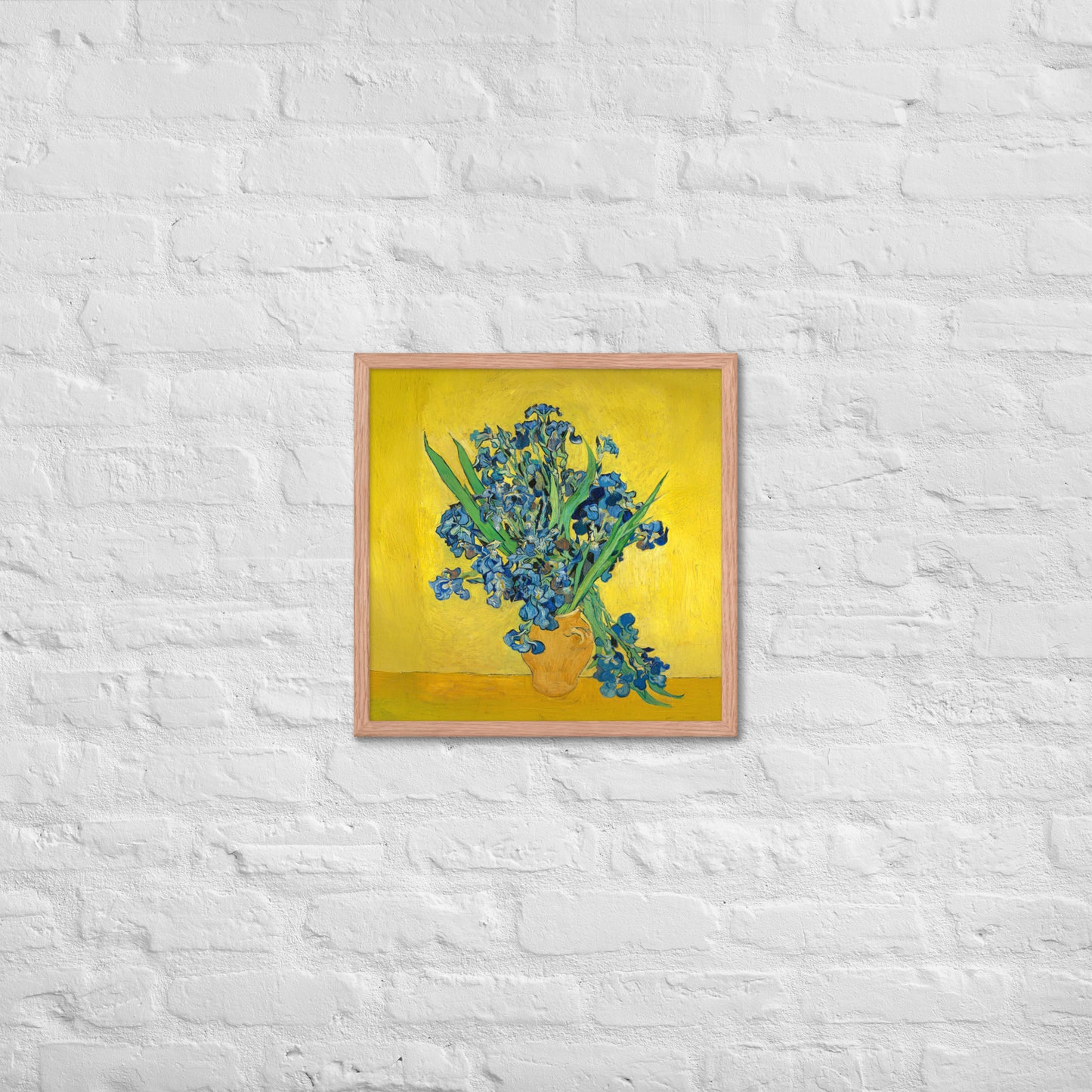 Van Gogh's 'Vase with Irises Against a Yellow Background' on a 18"x18" red oak framed poster print on a white brick wall.